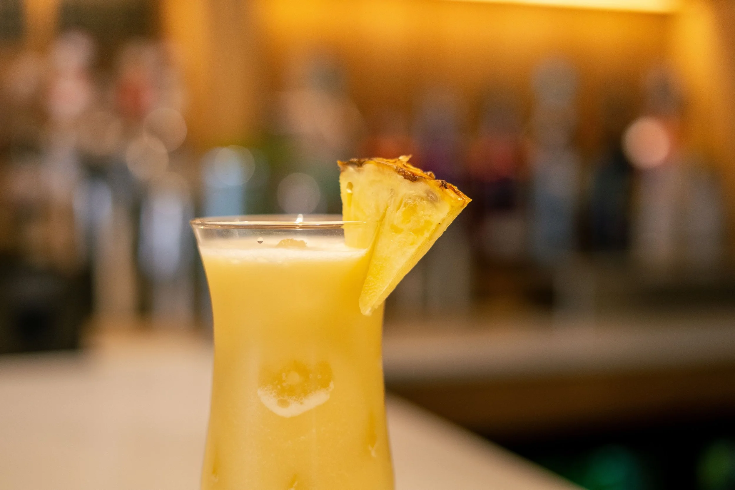 A tropical cocktail garnished with a pineapple slice on a blurred bar background.