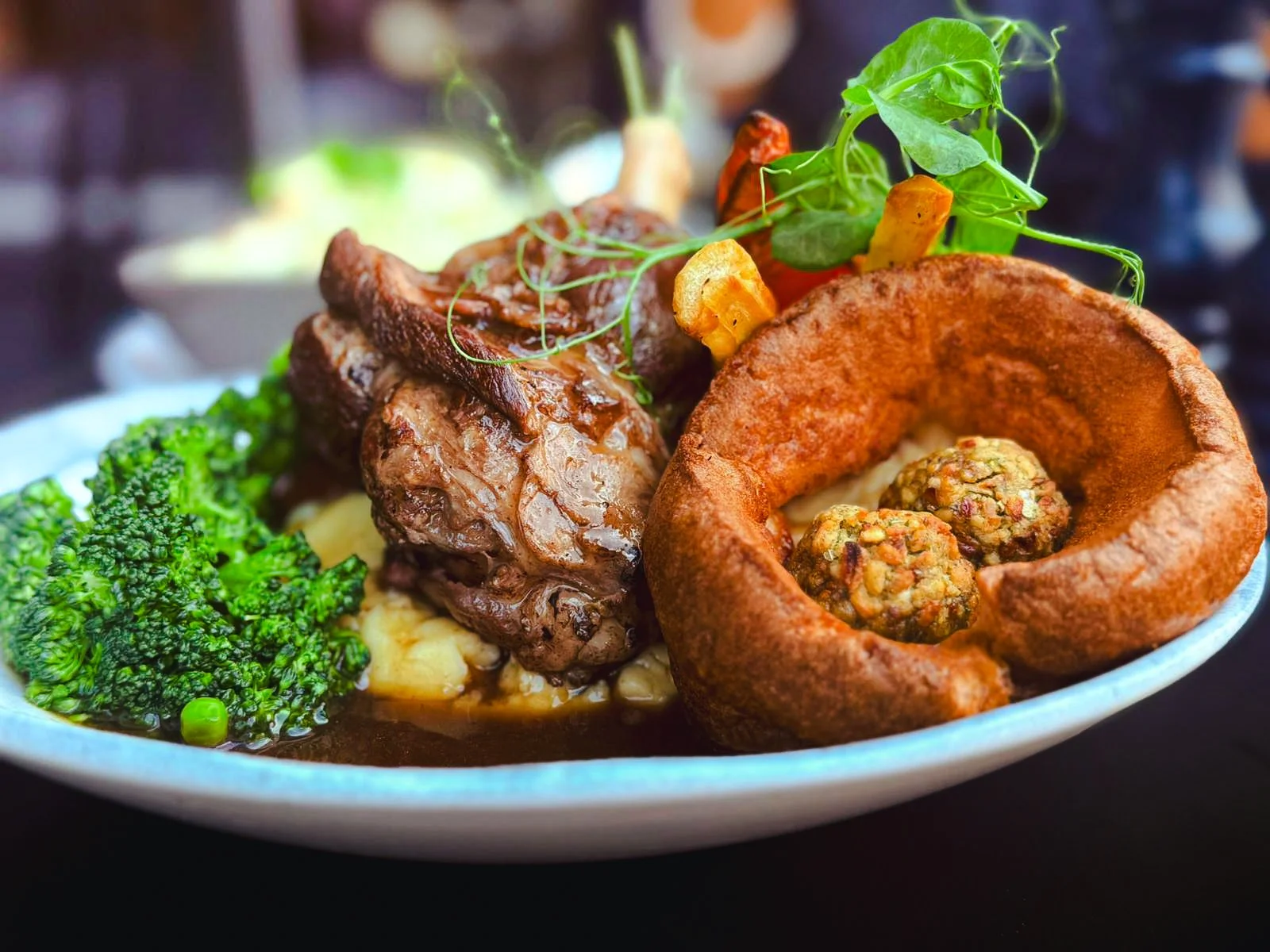 Plate of food with broccolini, grilled meat, and a bread bowl containing falafel balls garnished with microgreens.