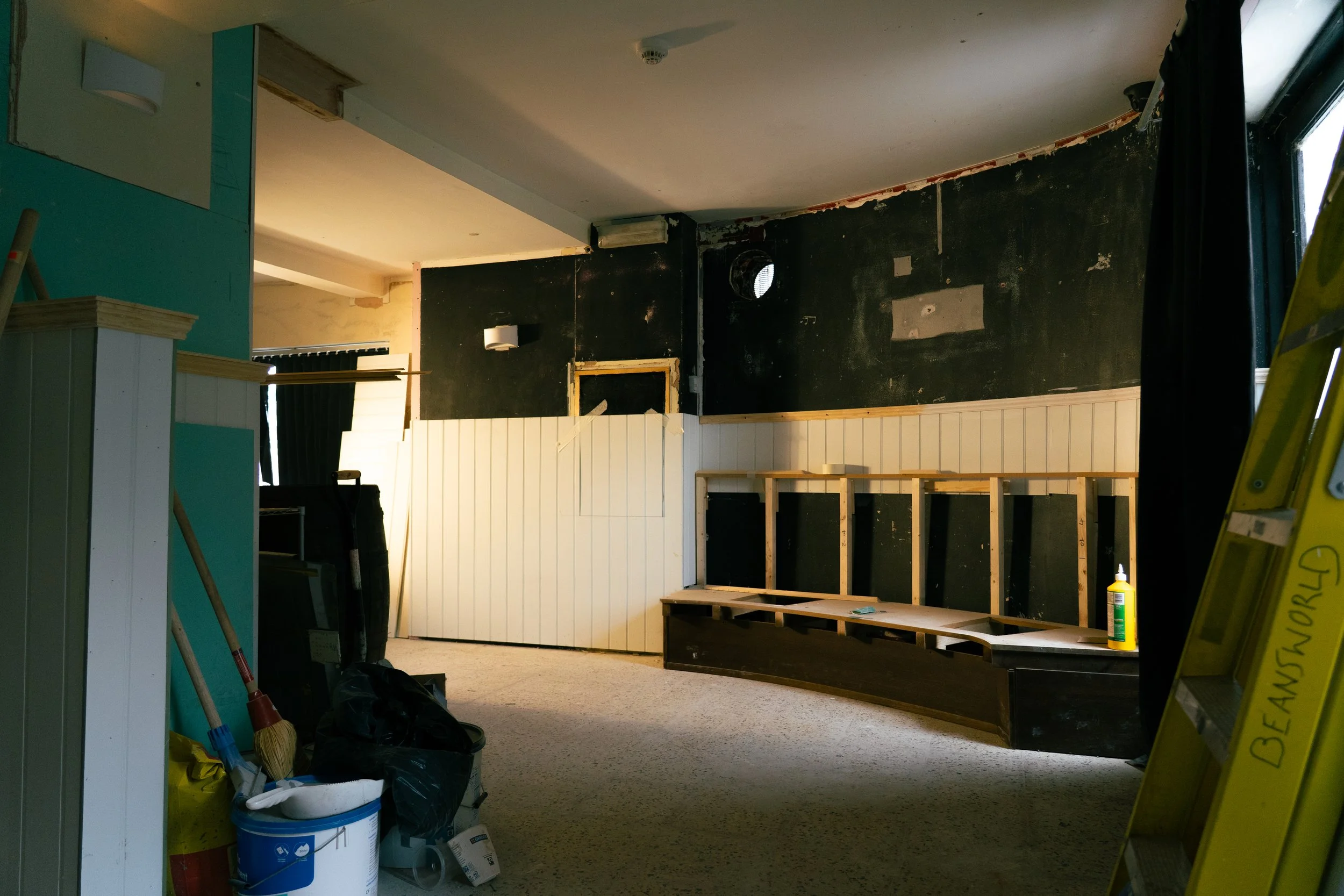 Interior space under renovation with construction materials, tools, and a partially built wall with wood paneling.