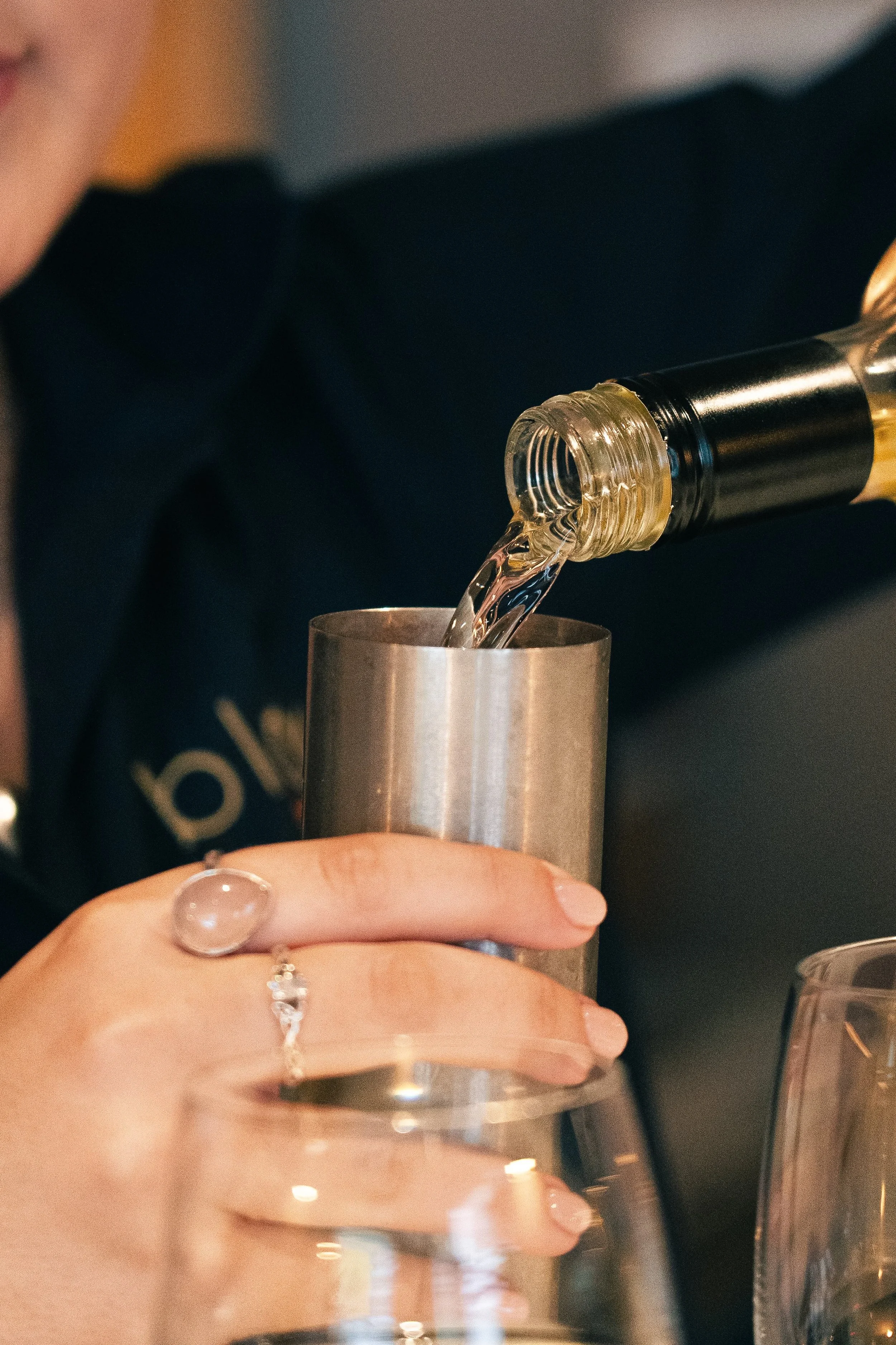 Person pouring a clear liquid from a black and gold bottle into a metallic cup