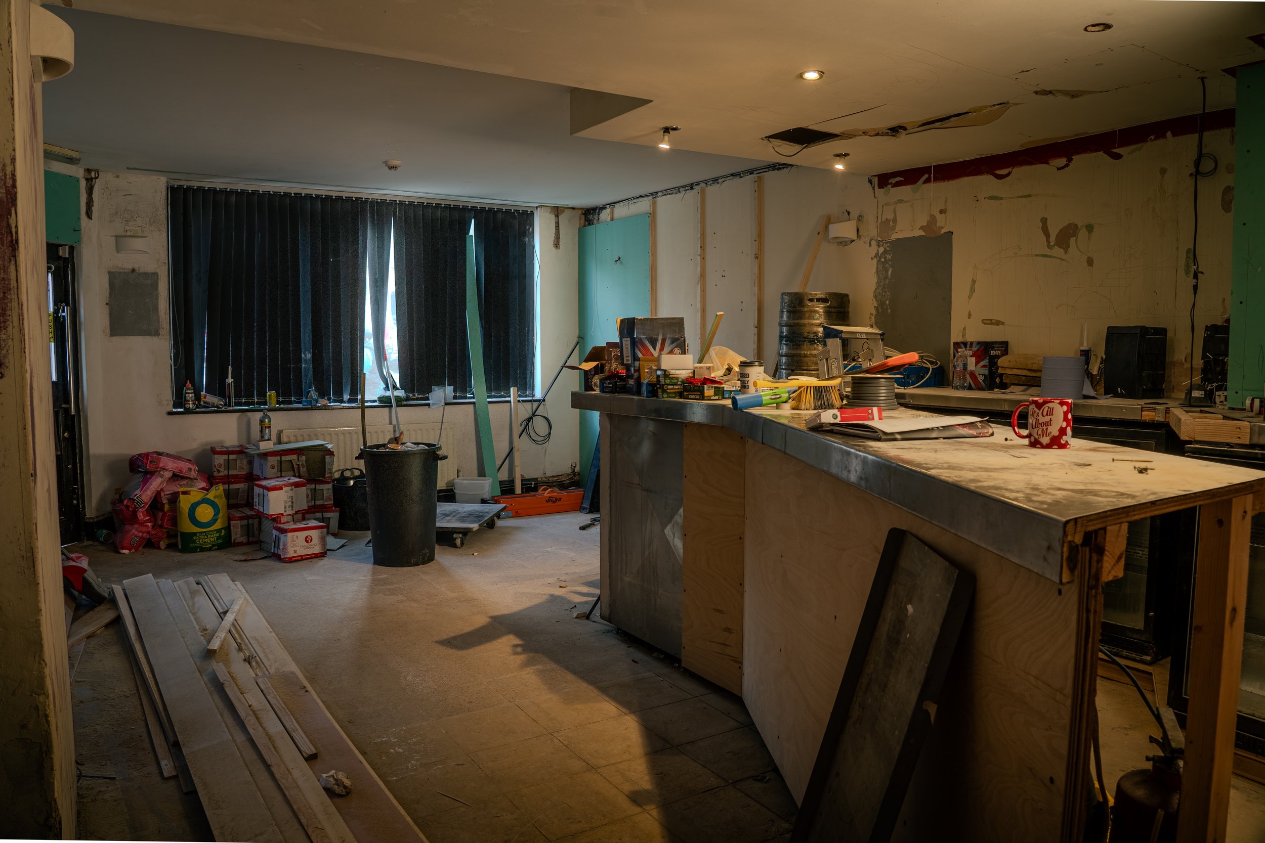 Under renovation room with construction tools and materials scattered, black curtains covering the window, and a makeshift counter with various items.
