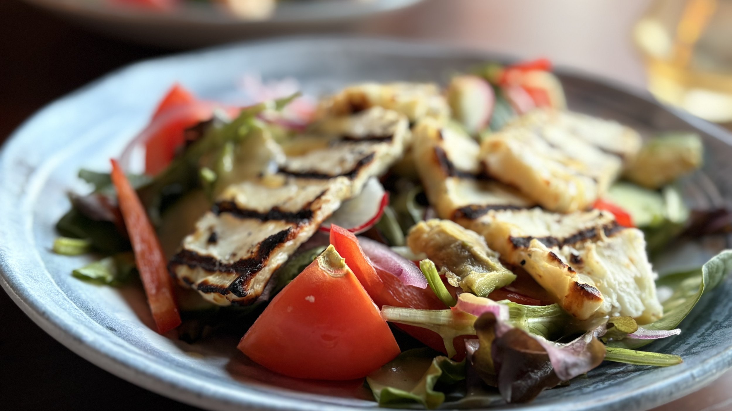 Grilled chicken with vegetables on a blue plate, including tomatoes, radishes, and leafy greens.