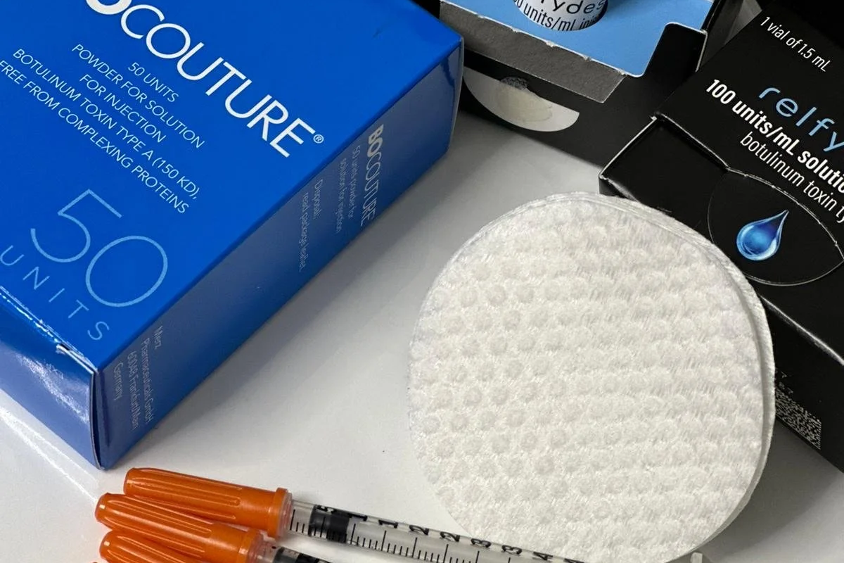 Medical supplies including two boxes of Botox and relfxy botulinum toxin, a white cotton pad, and three orange syringes.