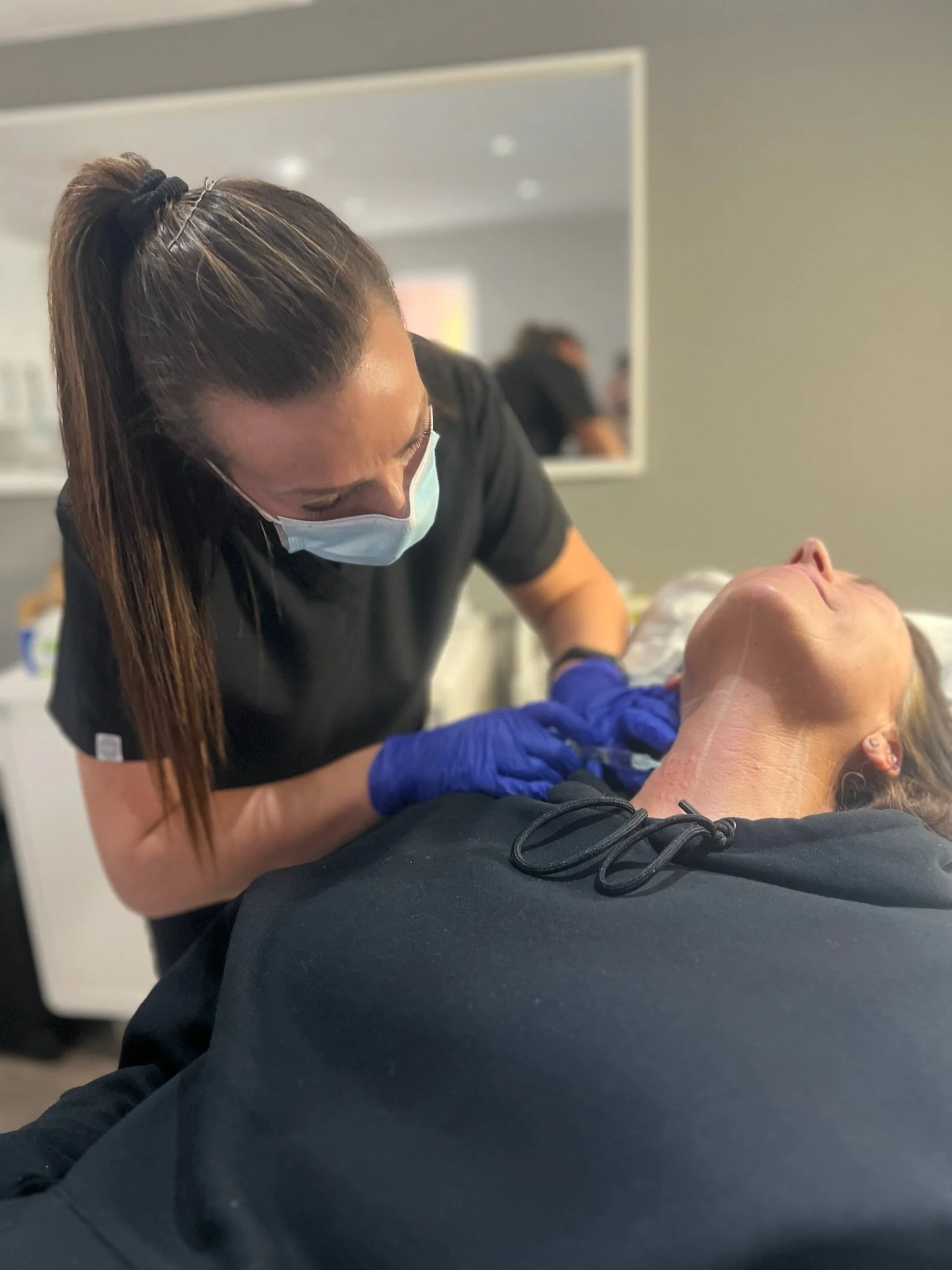 Elaine of Elaine Adams Aesthetics performing a cosmetic procedure on a person lying down in a clinical setting.