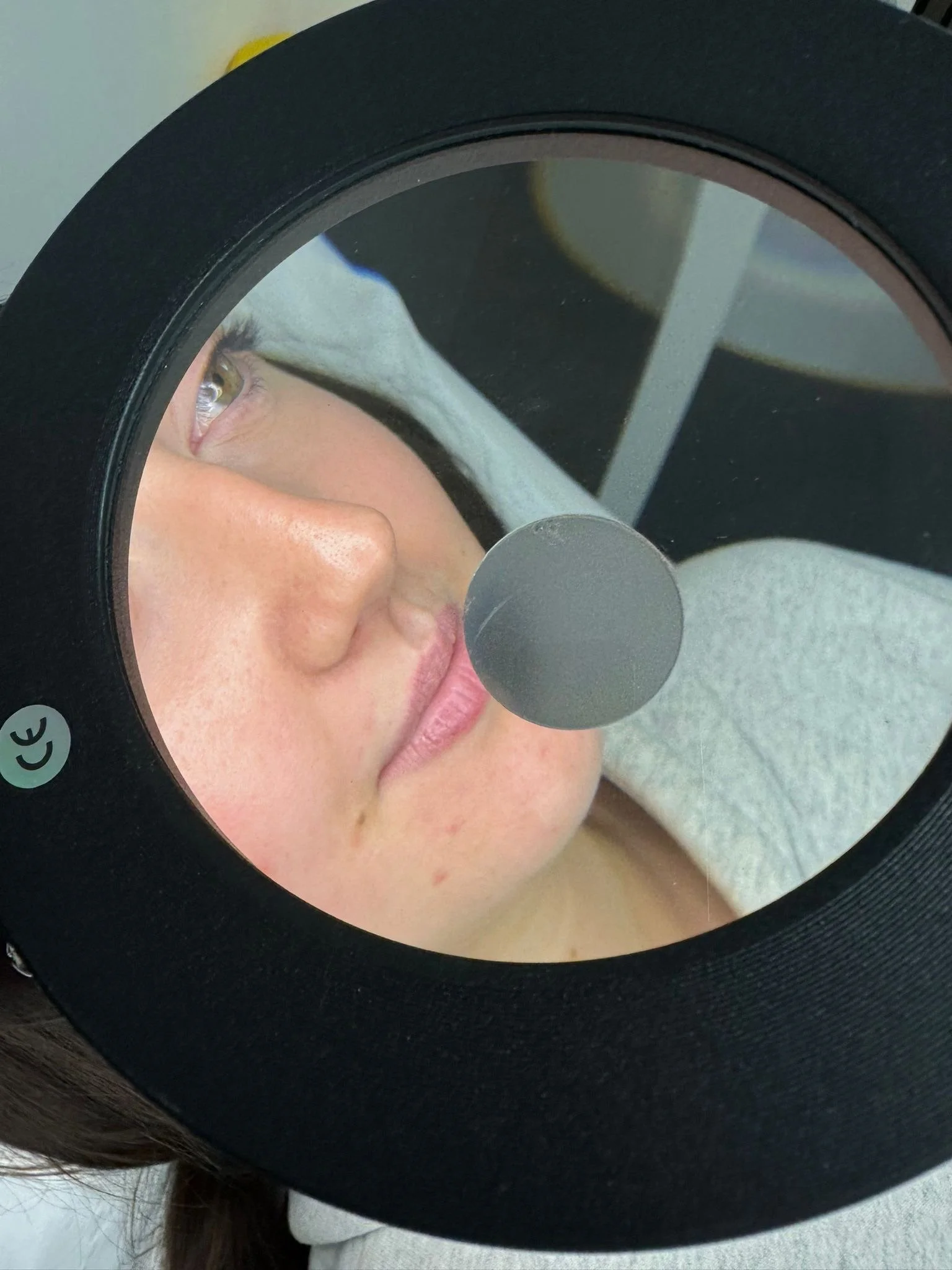 Close-up of a woman, examining or looking into a round black mirror with a reflective surface, showing part of her face, eye, and nose.