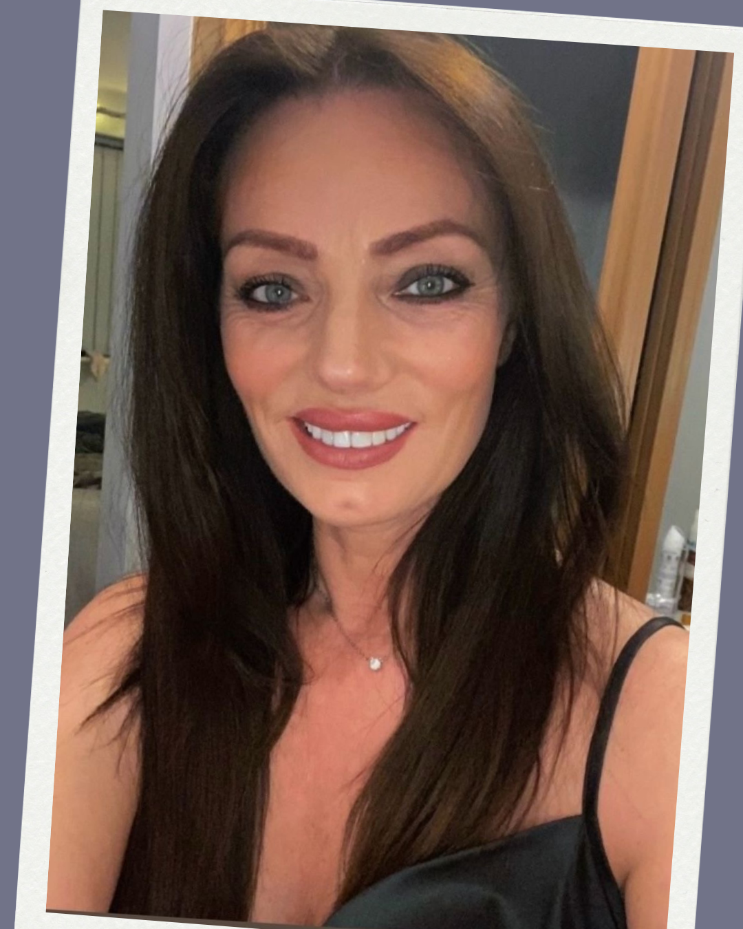 Close-up of Elaine of Elaine Adams Aesthetics - she is smiling and has long brown hair, blue eyes, wearing a black tank top and a delicate necklace.