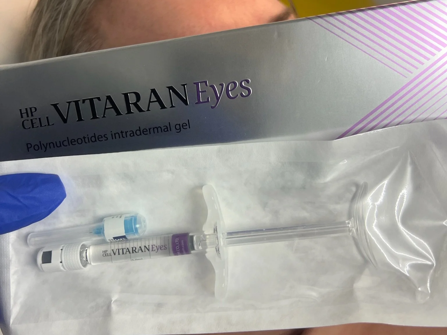 A syringe filled with a purple liquid labeled VITARAN Eyes, a small vial, and a pack of eye gel from HP CELL VITARAN Eyes, with purple and white packaging.