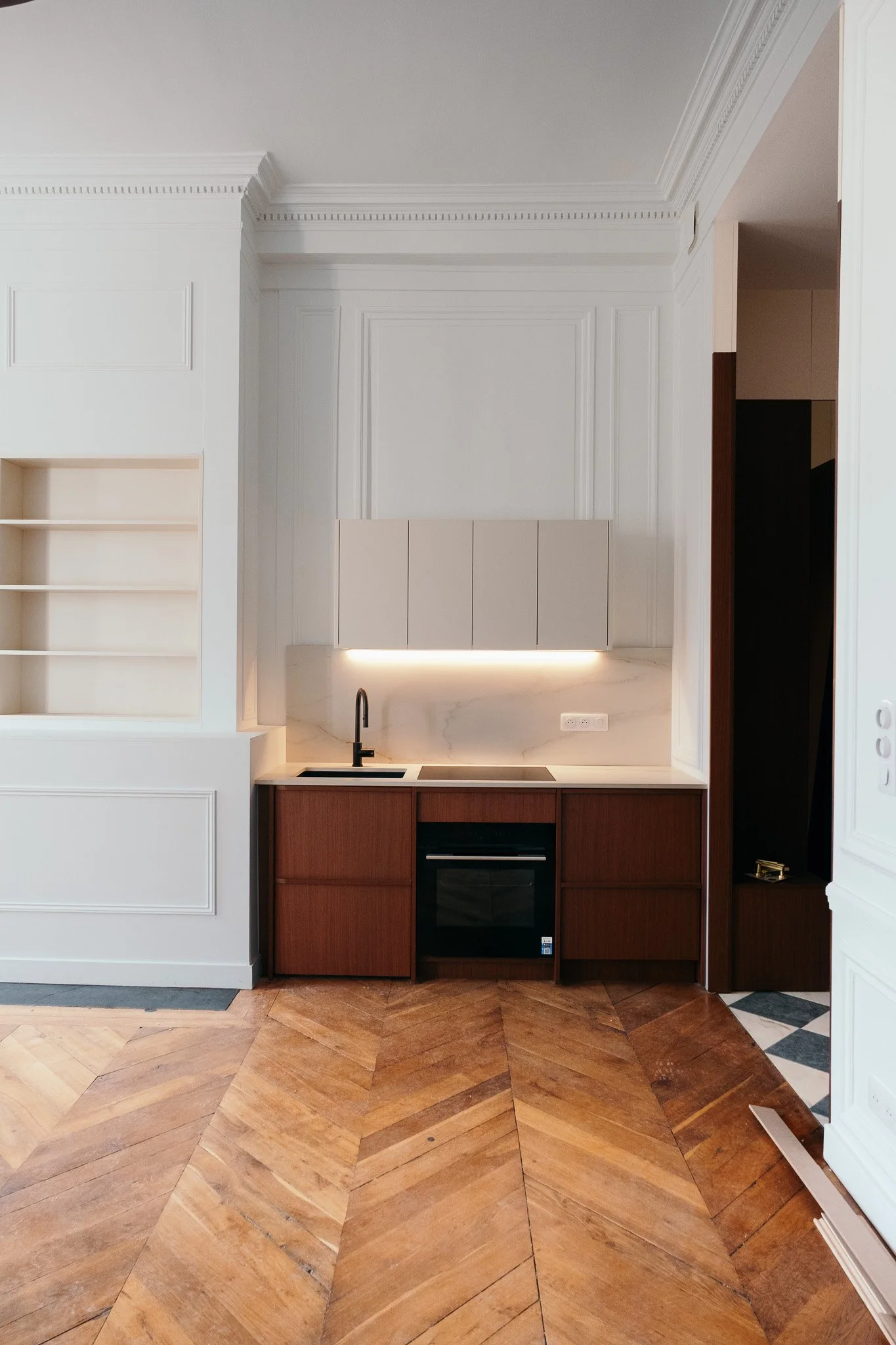 Cuisine moderne avec plan de travail en marbre, armoires blanches, four encastré, sol en parquet.
