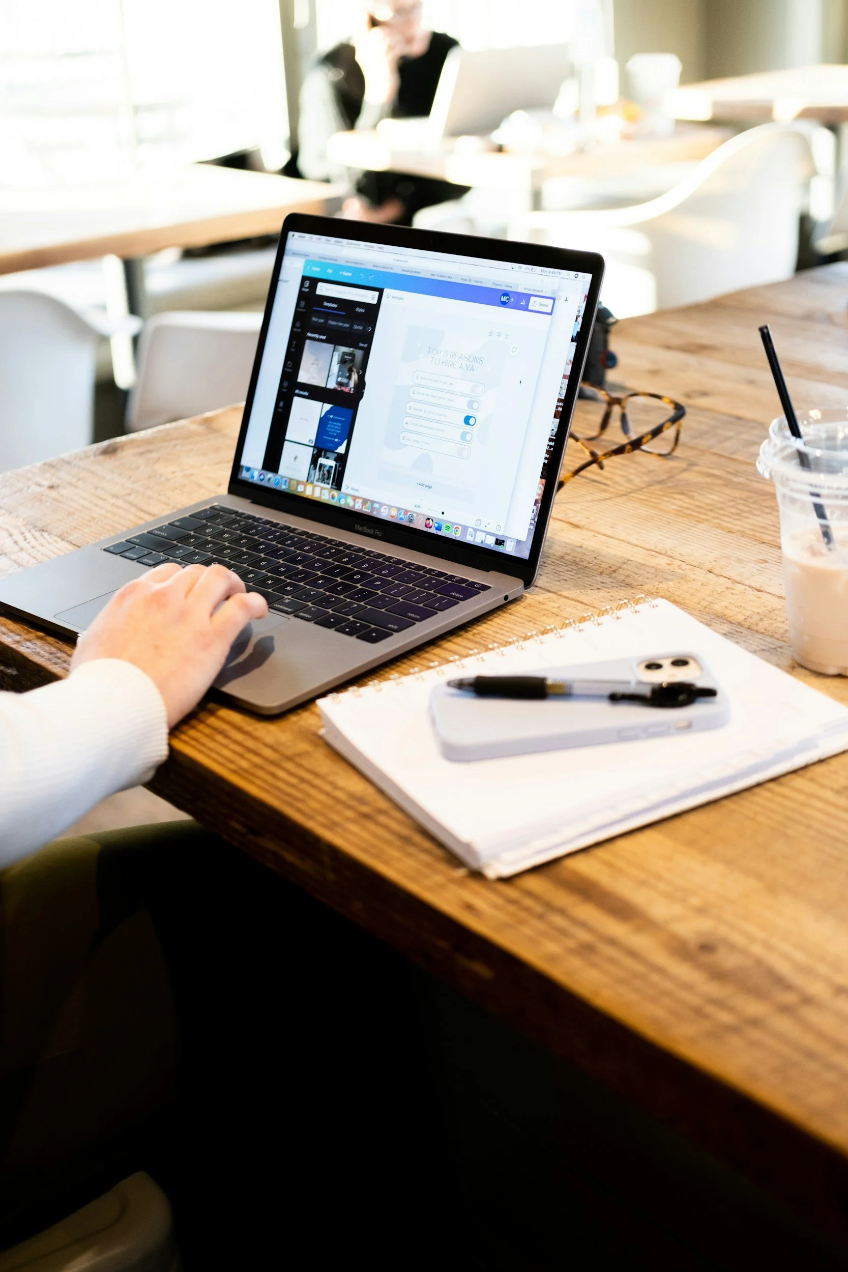 A person working on a laptop office space. The laptop screen displays a presentation or infographic. There is a notebook and a pen. They are working on allied health admin projects to support clinics.