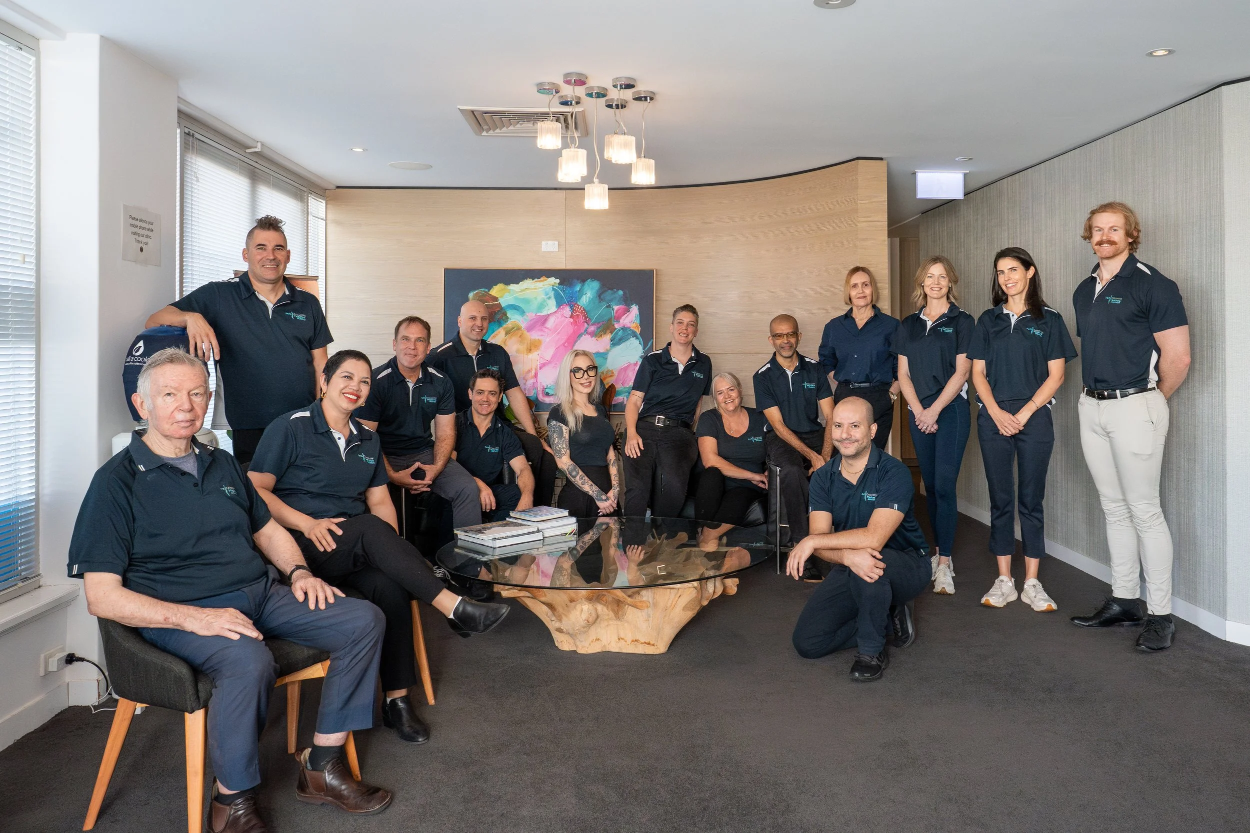 Group photo of all the practitioners at Perth Osteopathic Medicine and Podiatry including Podiatrists, Osteopaths, Remedial Massage Therapists and Receptionists all wearing branded business shirts in Nedlands Perth WA