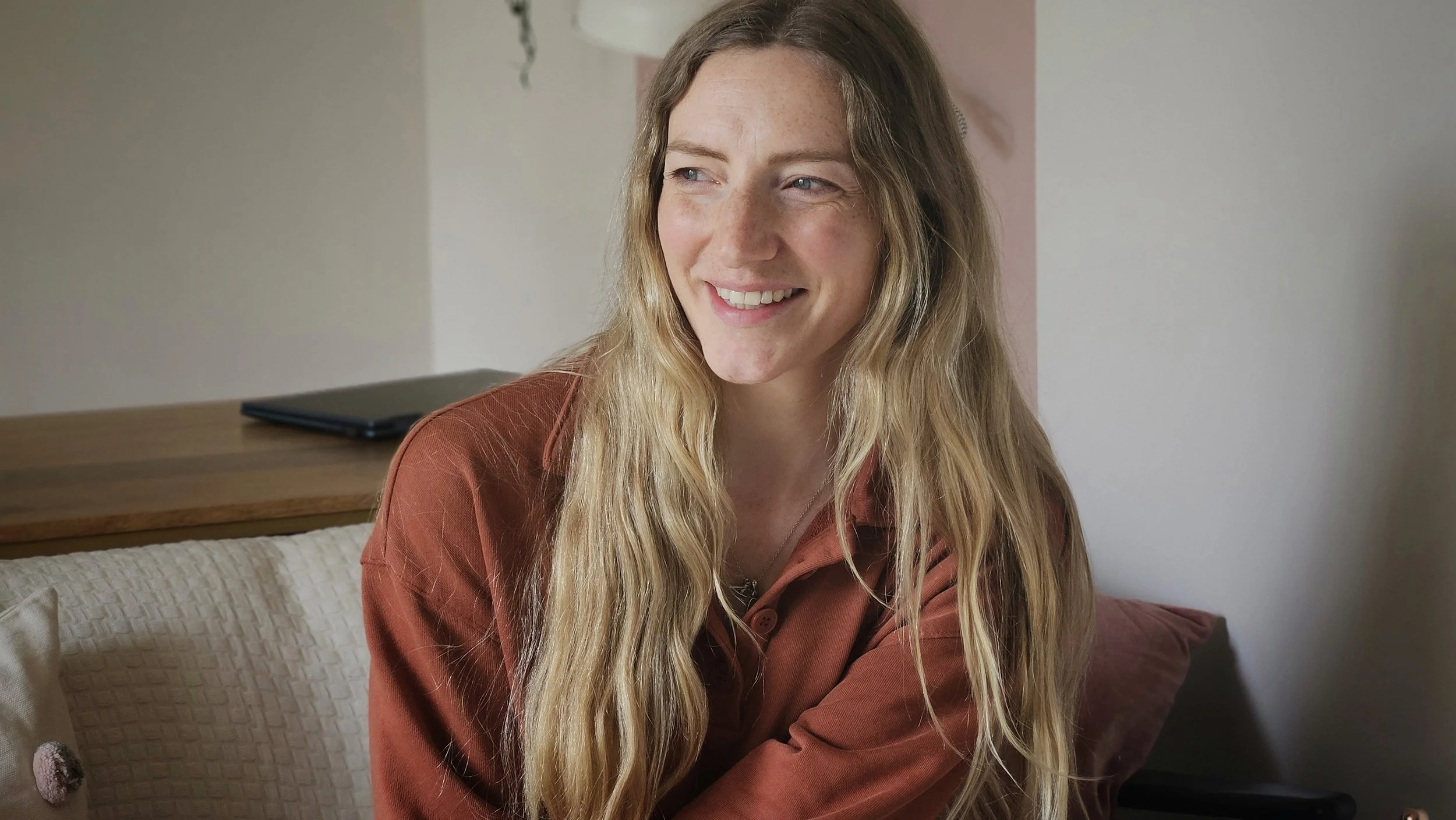 A smiling woman with long blond hair sitting in the garden office of Nourish and Flourish in Halifax