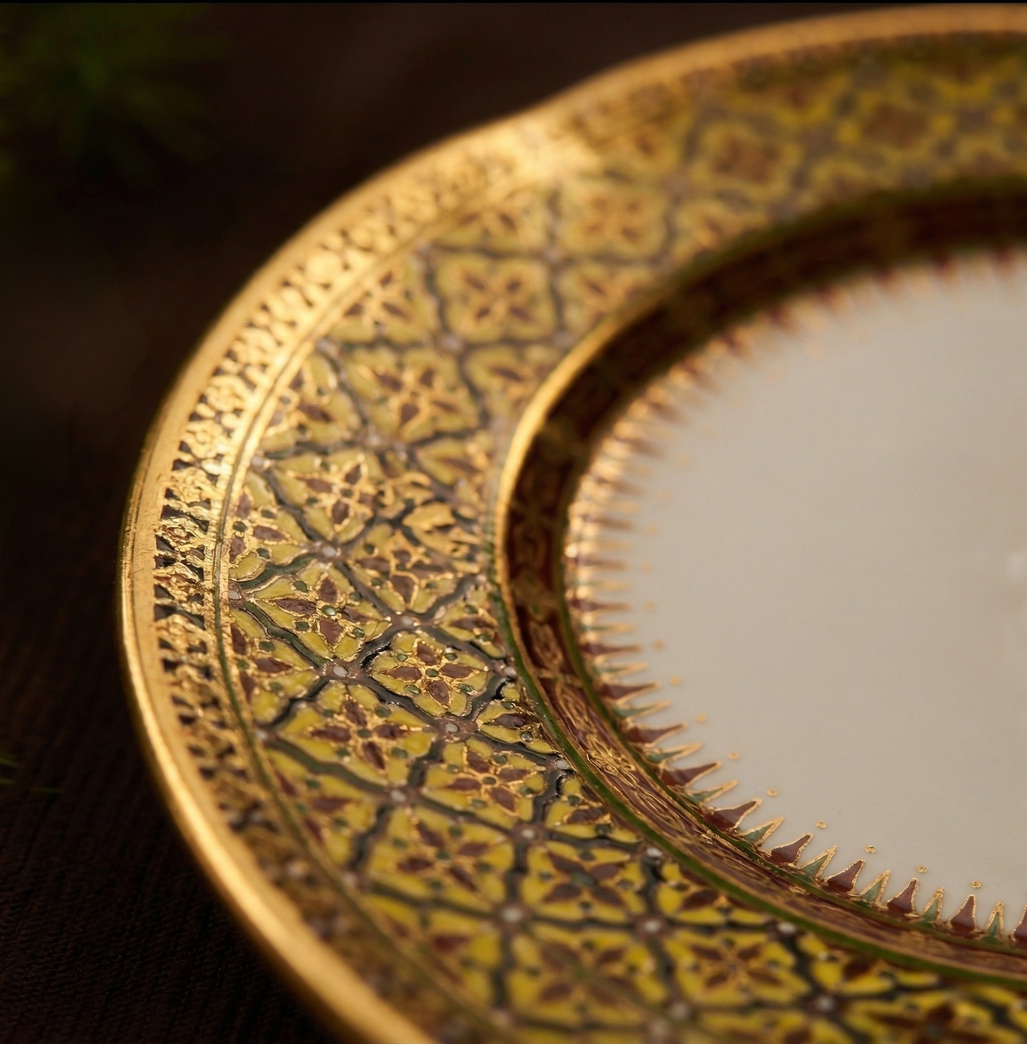 Close-up of a decorative, gold-colored, intricately patterned object with curved edges and spiked details along the border.