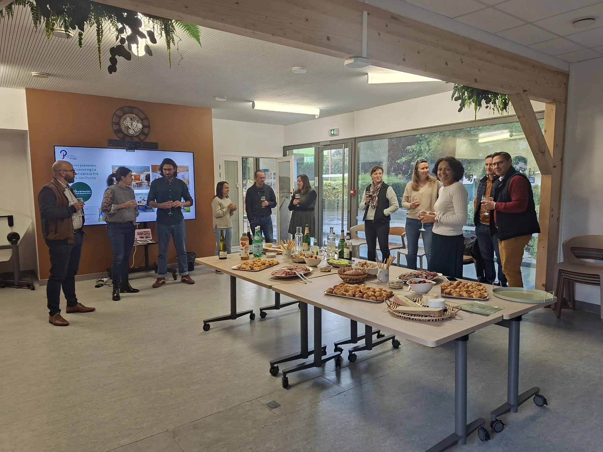 Groupe de personnes discutant lors d'une réunion ou d'une fête d'entreprise avec un buffet de nourriture à l'avant-plan dans une salle moderne avec grandes fenêtres.