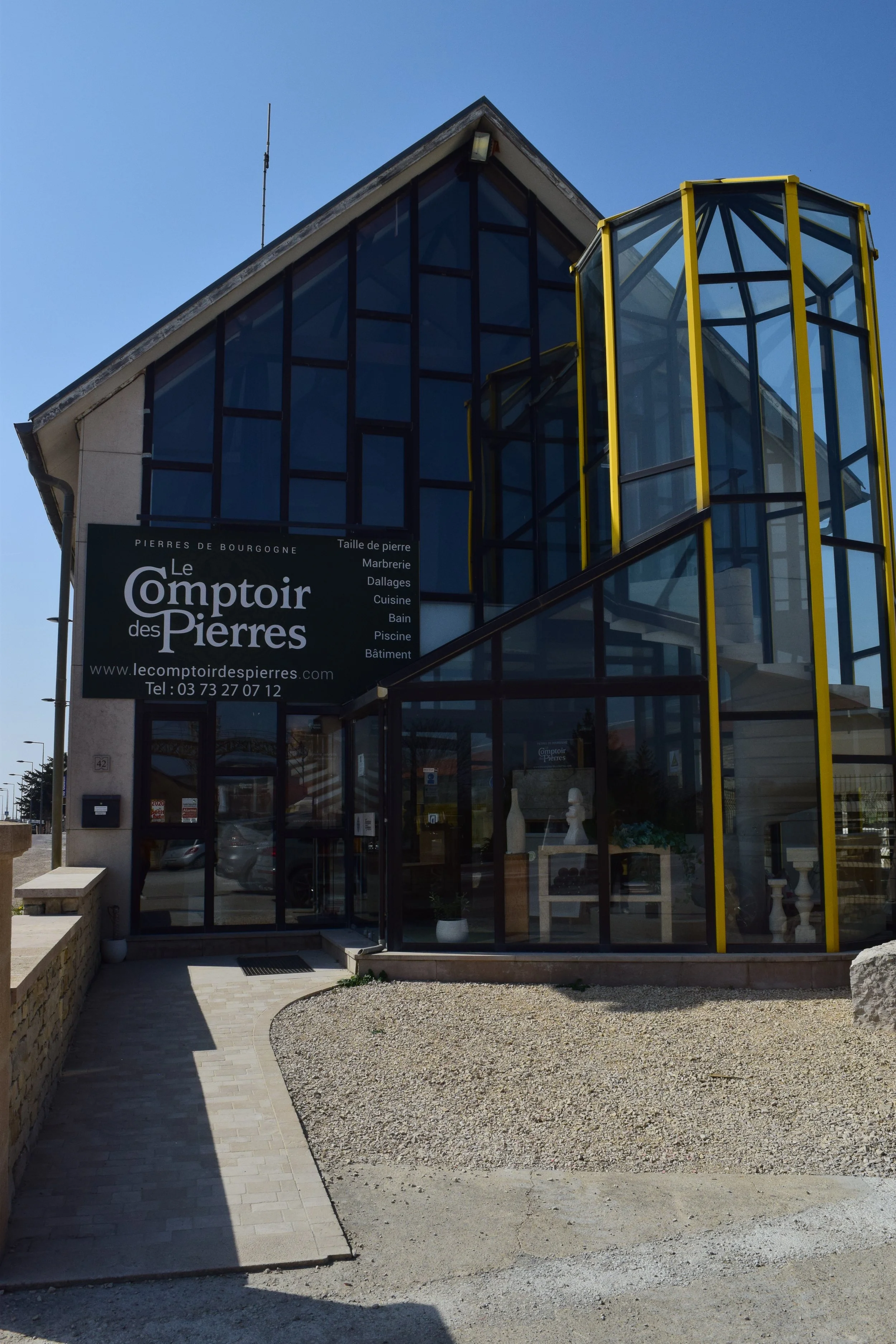 Façade d'un bâtiment moderne avec la enseigne 'Le Comptoir des Pierres' et une entrée principale en verre.