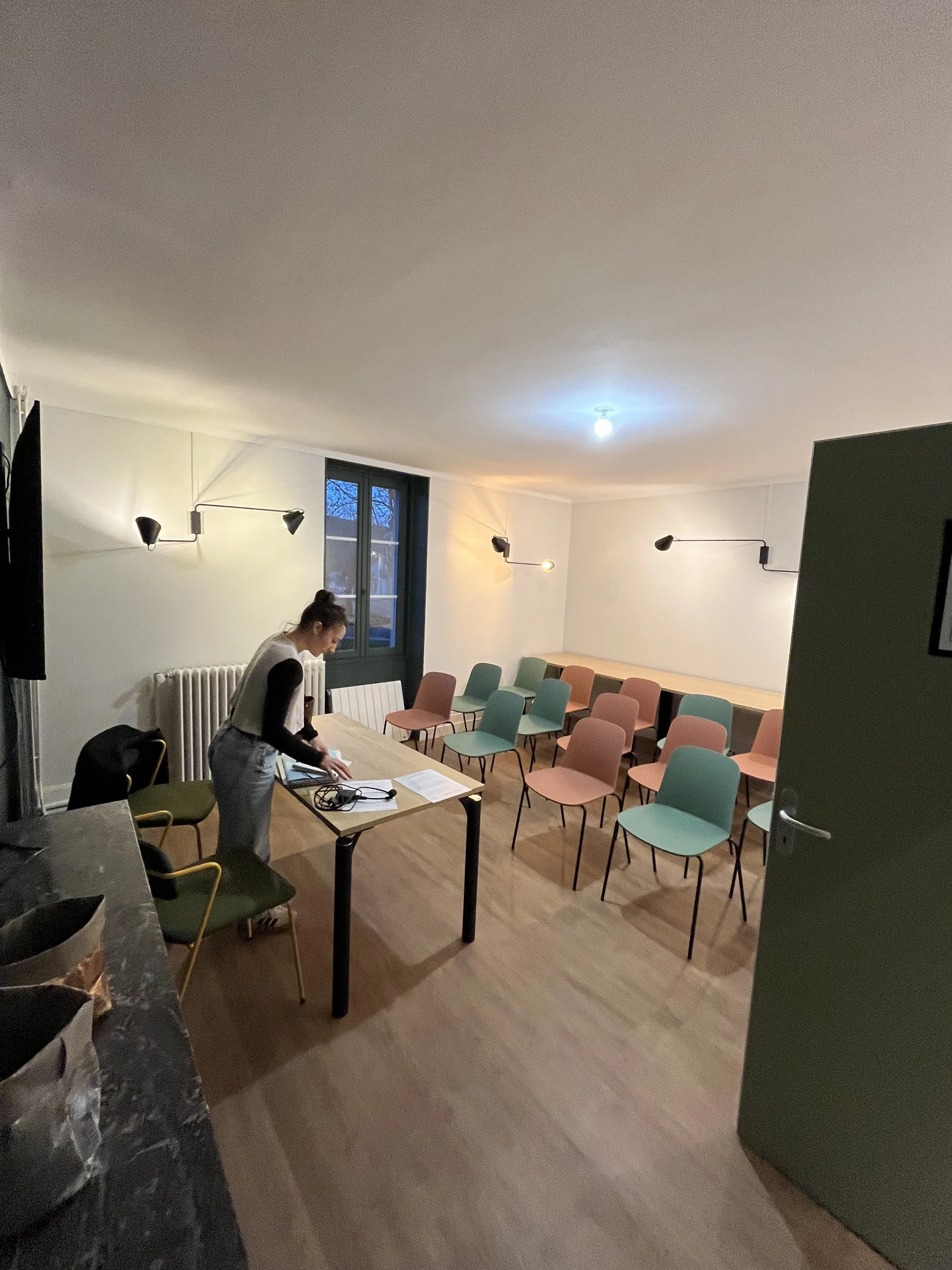 Une salle de réunion avec des chaises de différentes couleurs, un tableau, et plusieurs personnes préparant le matériel.