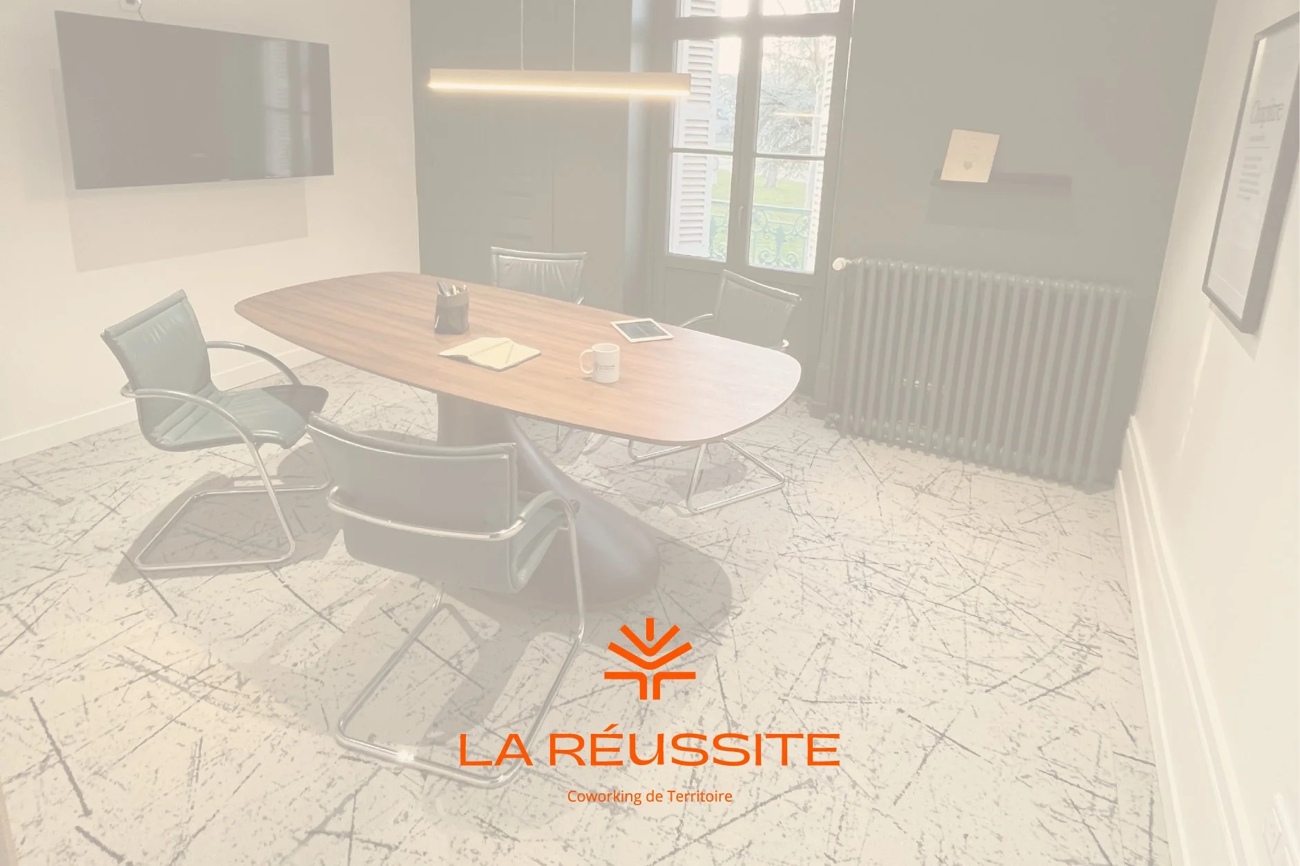 Une salle de réunion avec une grande table en bois, des chaises en cuir noir autour, une fenêtre avec des volets en arrière-plan, une télévision au mur, une lampe suspendue, un ordinateur portable, une tablette, une tasse, et du papier. Le sol est en marbre clair avec des veines sombres. Le logo "LA REUSSITE" et le texte "Coworking de Territoire" sont superposés.