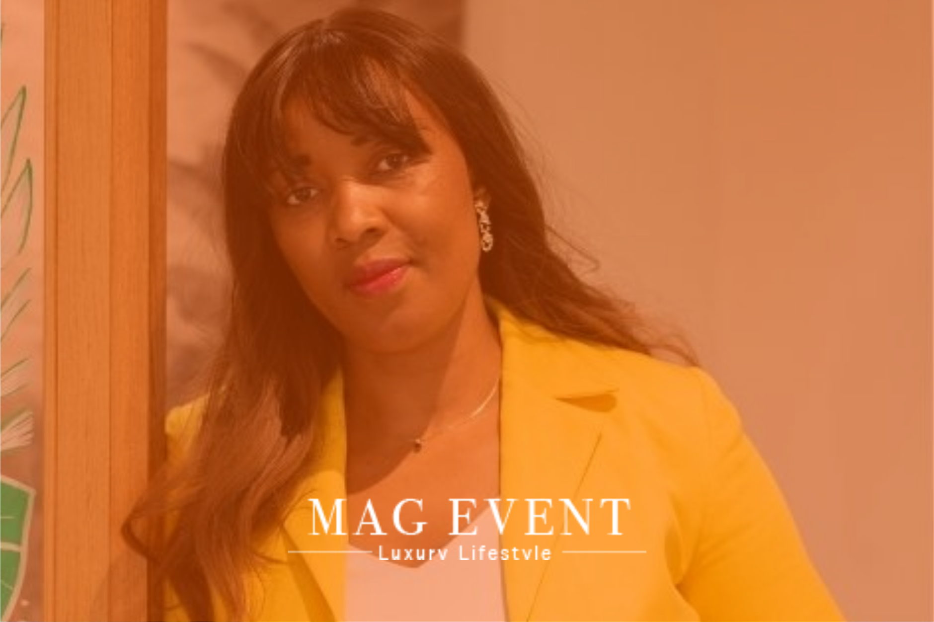 Une femme souriante avec des cheveux longs et bruns portant une robe jaune, posant à côté d'une porte en bois dans une pièce lumineuse. Texte sur l'image : "MAG EVENT - Luxe Lifestyle".