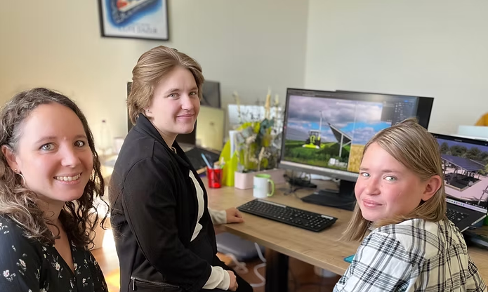 Trois femmes assises à un bureau avec deux écrans d'ordinateur affichant des images de construction ou de design architectural.