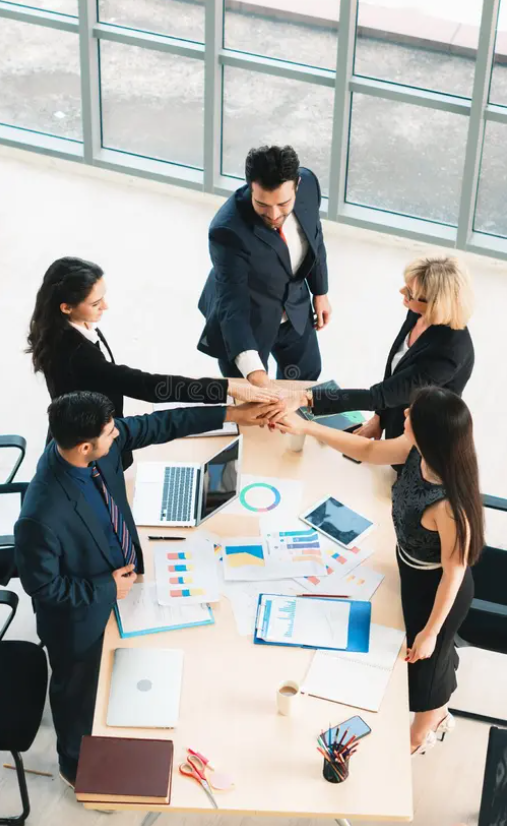 Business team in a modern office shrugging hands in a group hug