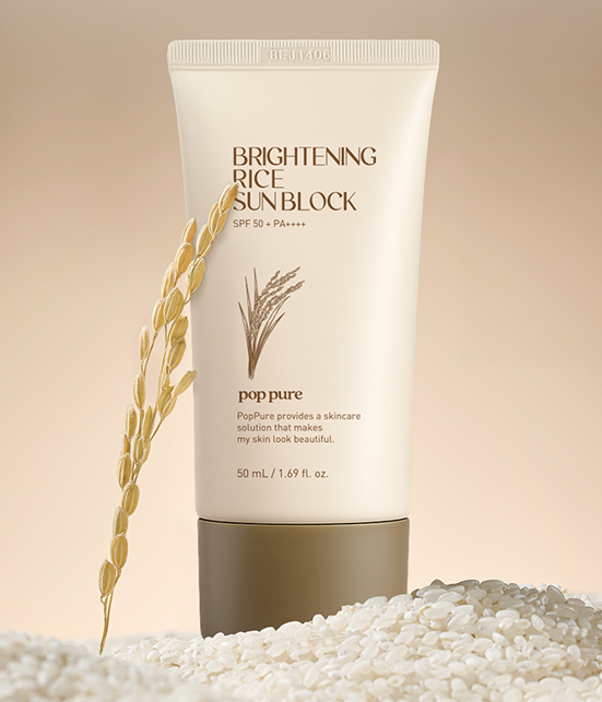 A bottle of Brightening Rice Sunblock next to rice grains, with a rice stalk leaning against it.