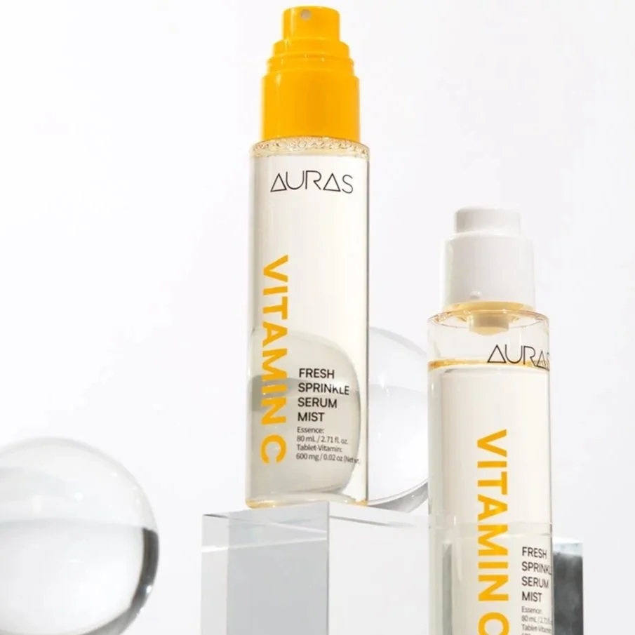 Two bottles of Aurora Vitamin C serum and mist on platforms with clear background, one with a yellow pump, both featuring white and yellow labels