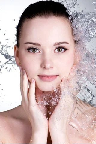 A woman with clear skin surrounded by splashes of water and ice, looking directly at the camera.