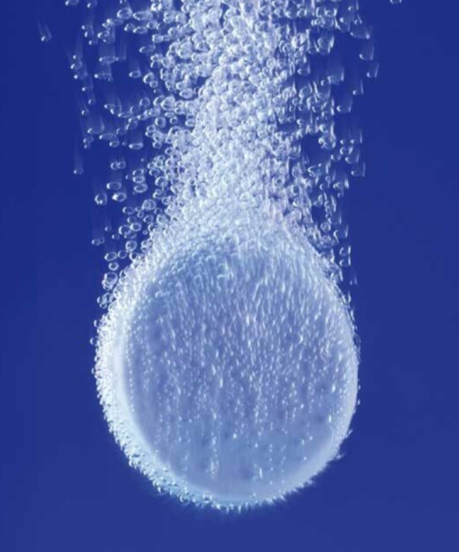 A close-up image of a bubble rising in water with many smaller bubbles around it against a blue background.
