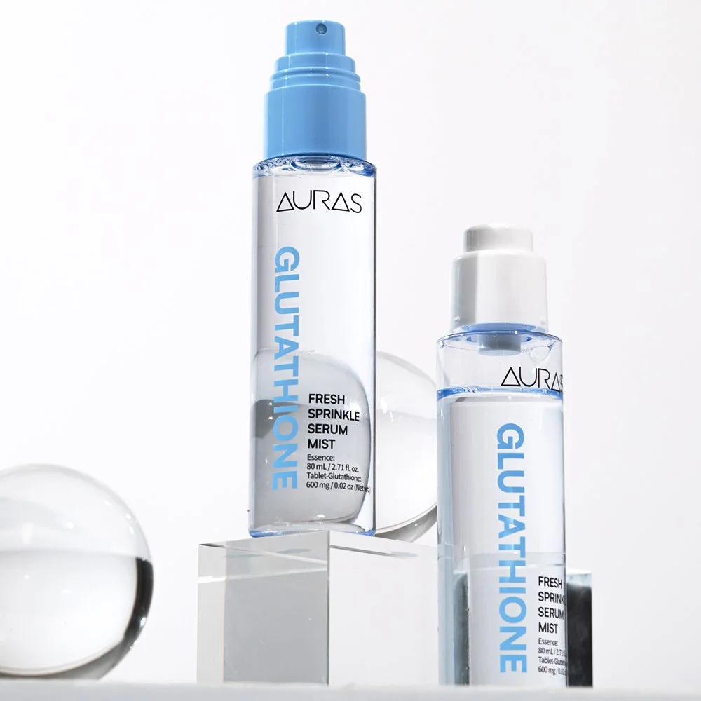 Two bottles of Aura Glutathione Fresh Spritzle Serum Mist on clear geometric display with soft lighting and reflection.