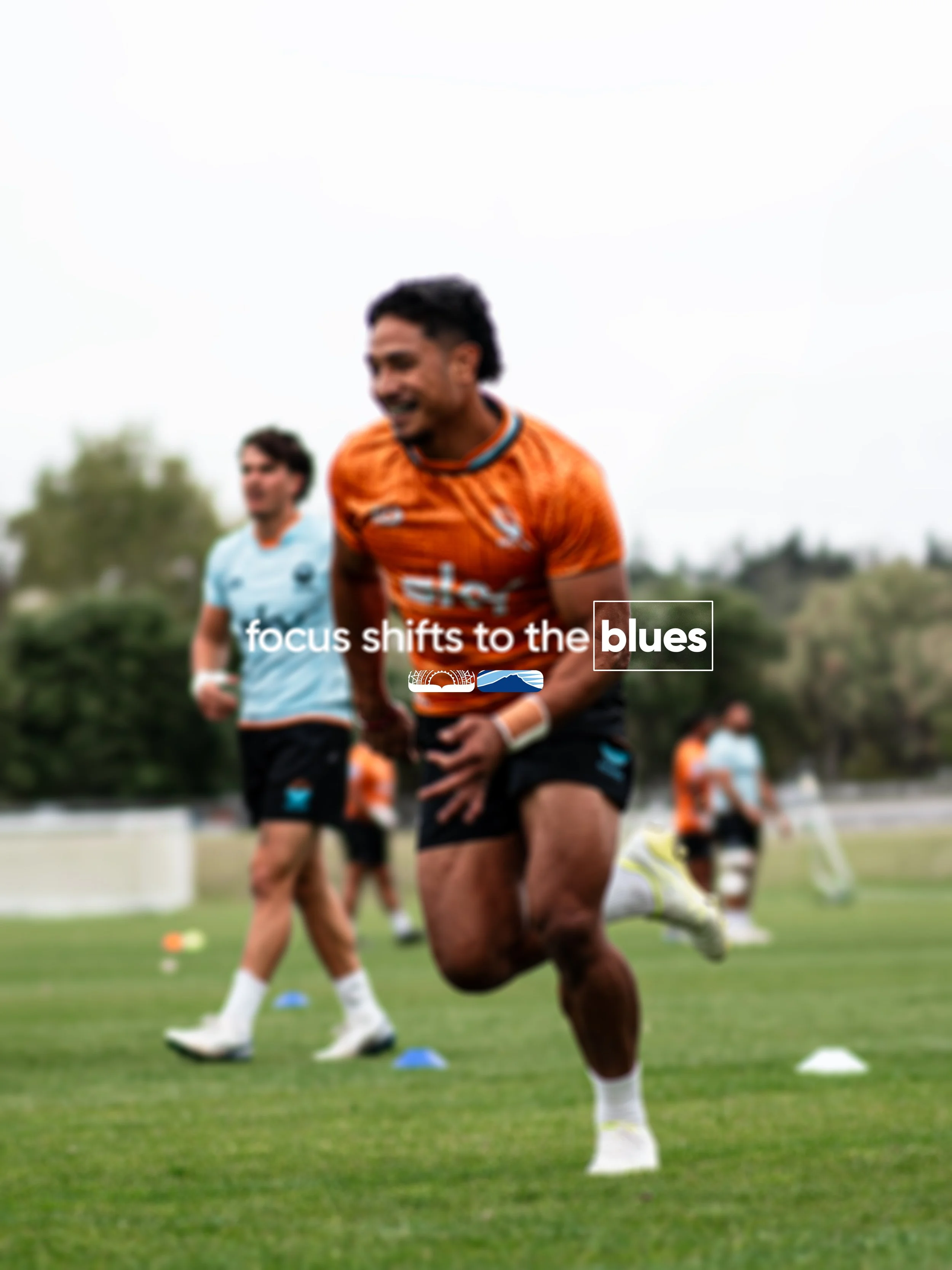 A group of rugby players running on a field during training or practice, with trees and hills in the background.