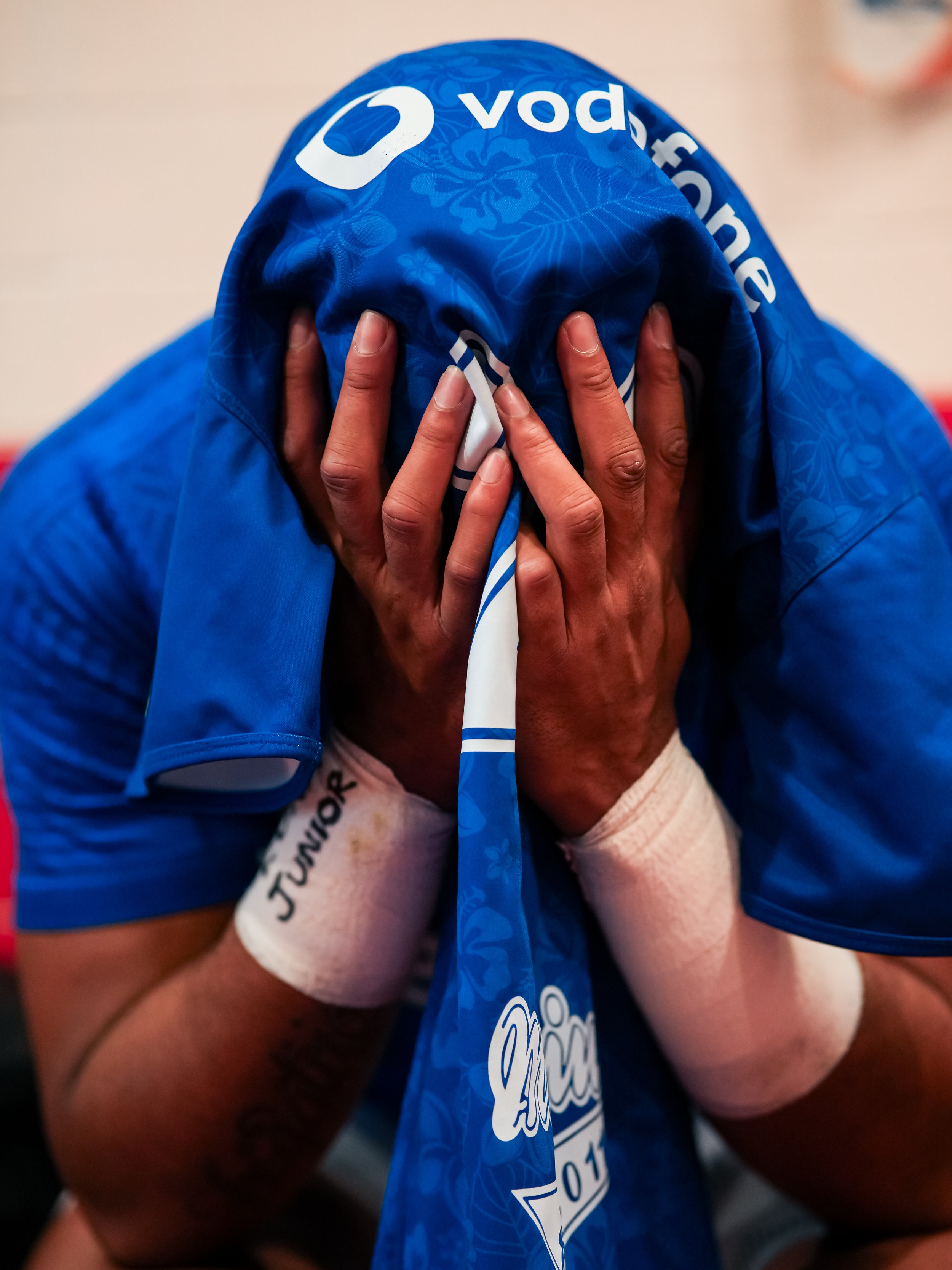 A person with hands clasped in front of their face, praying into their rugby jersey.
