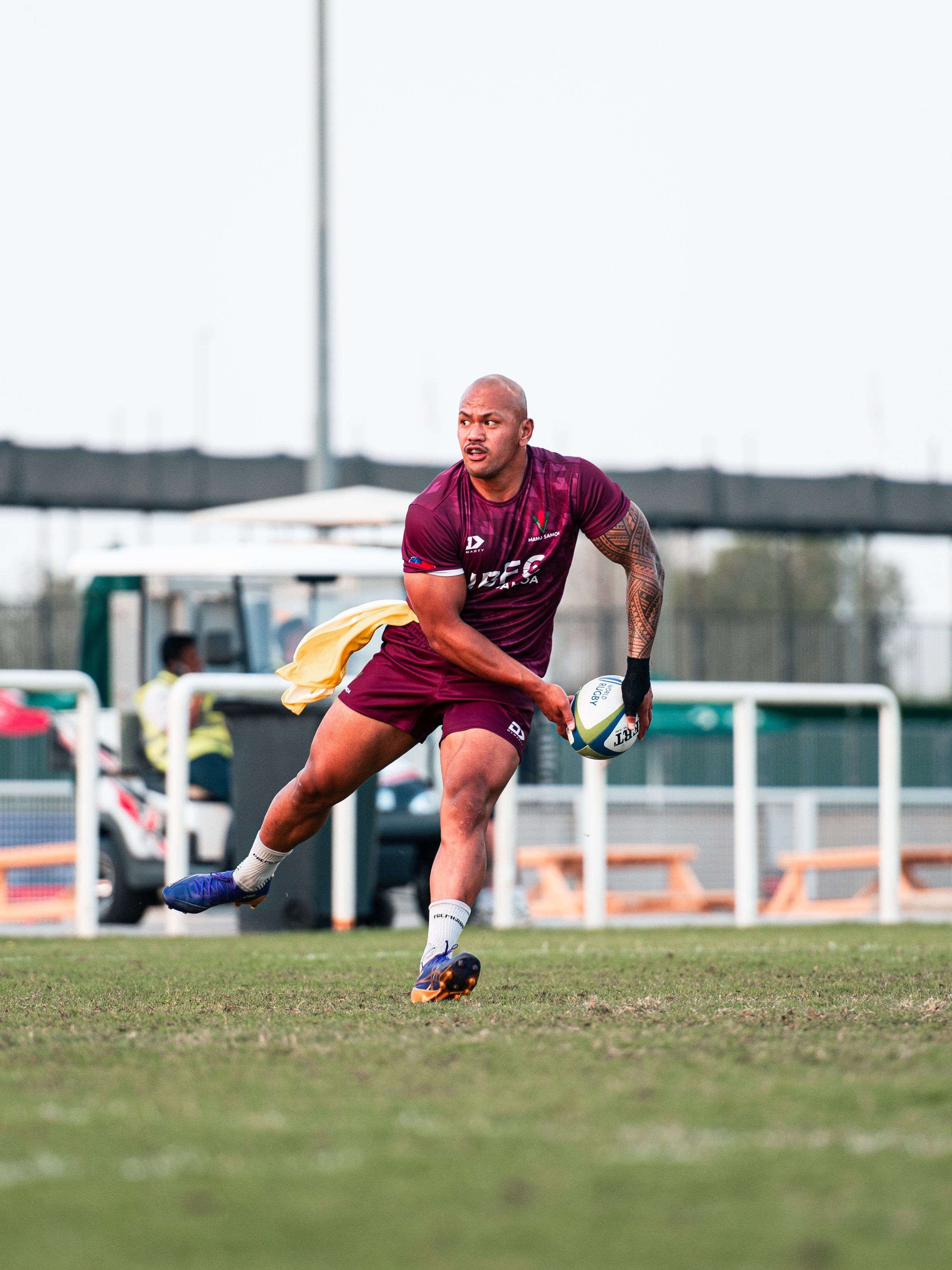 A rugby player in maroon uniform running on the field with a rugby ball in his hand during a game.