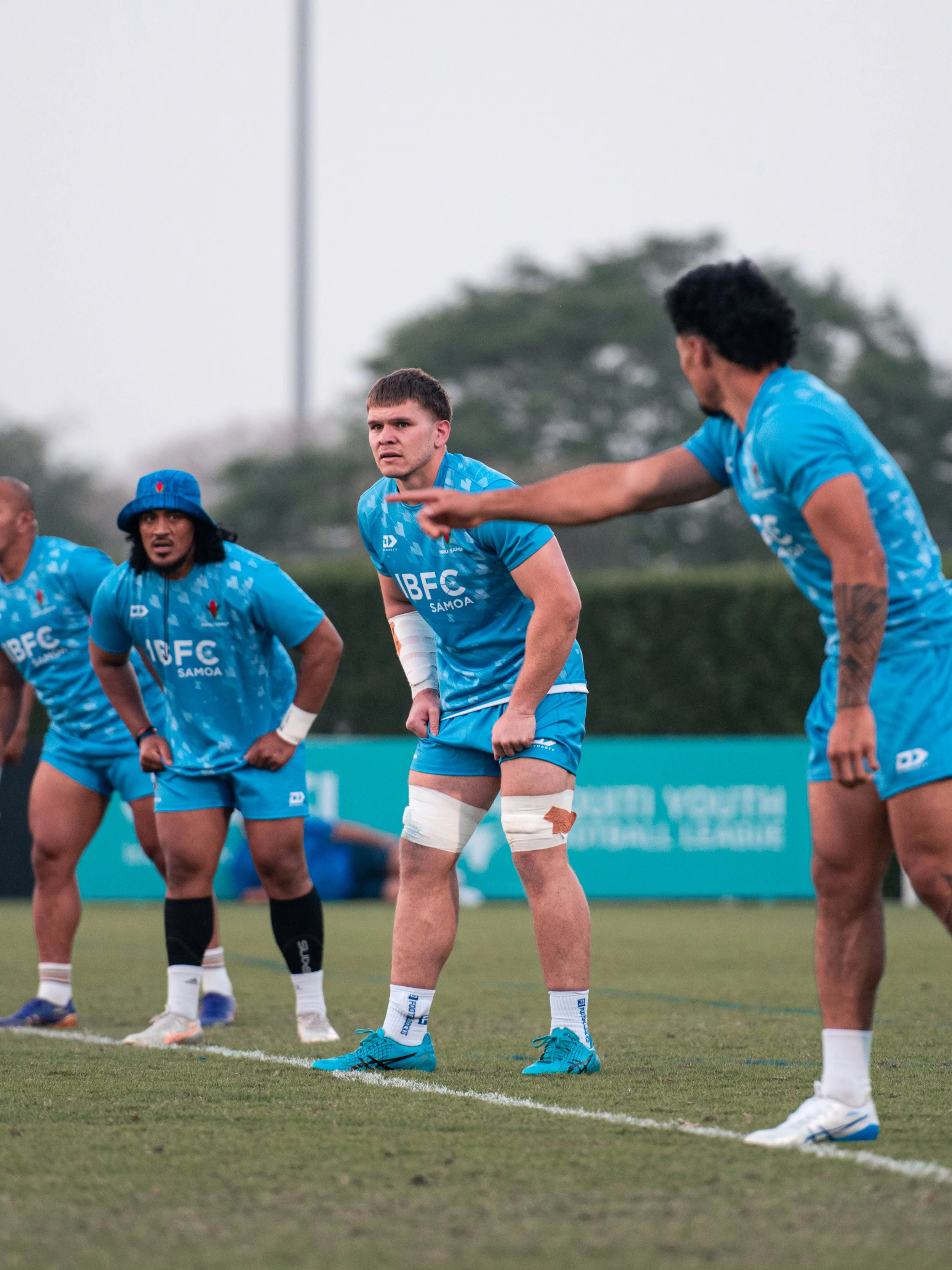 Four rugby players in blue uniforms standing on a grassy field during a game, focusing on a player with a bandaged leg.