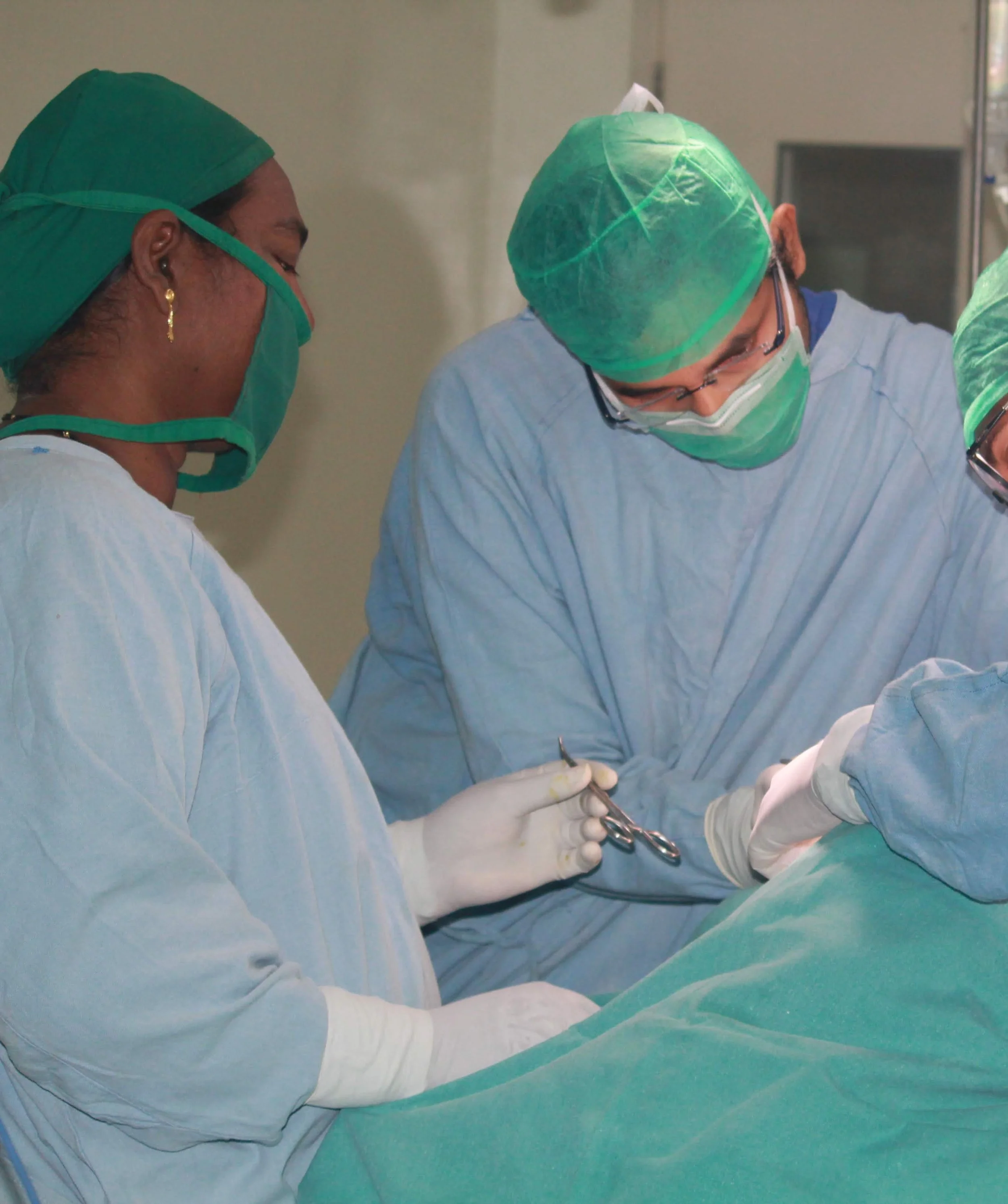 Medical professionals in scrubs, masks, and gloves performing surgery in an operating room.