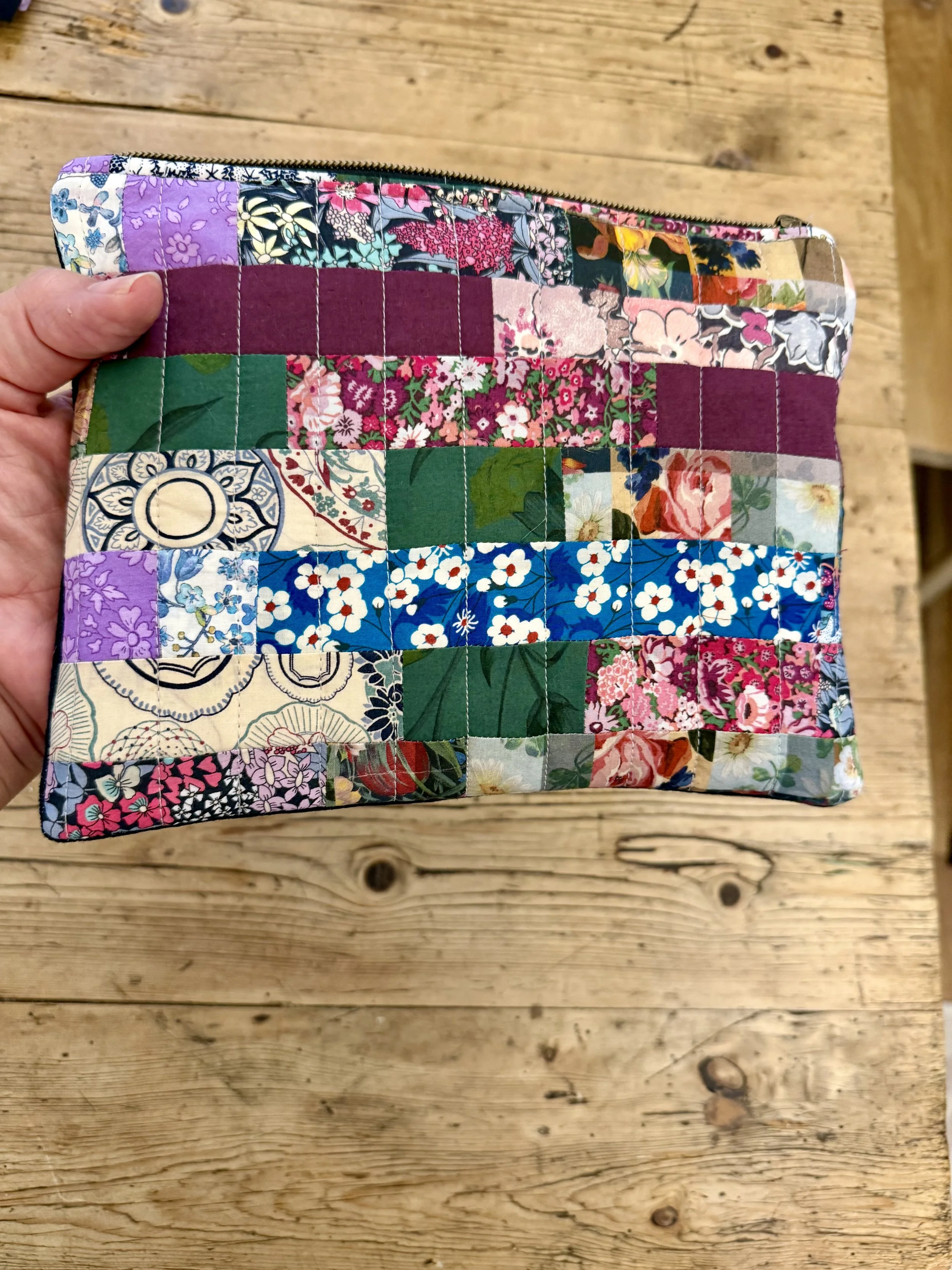 1. Hand holding colourful Liberty Scrapbook Patchwork Pouch showing its size