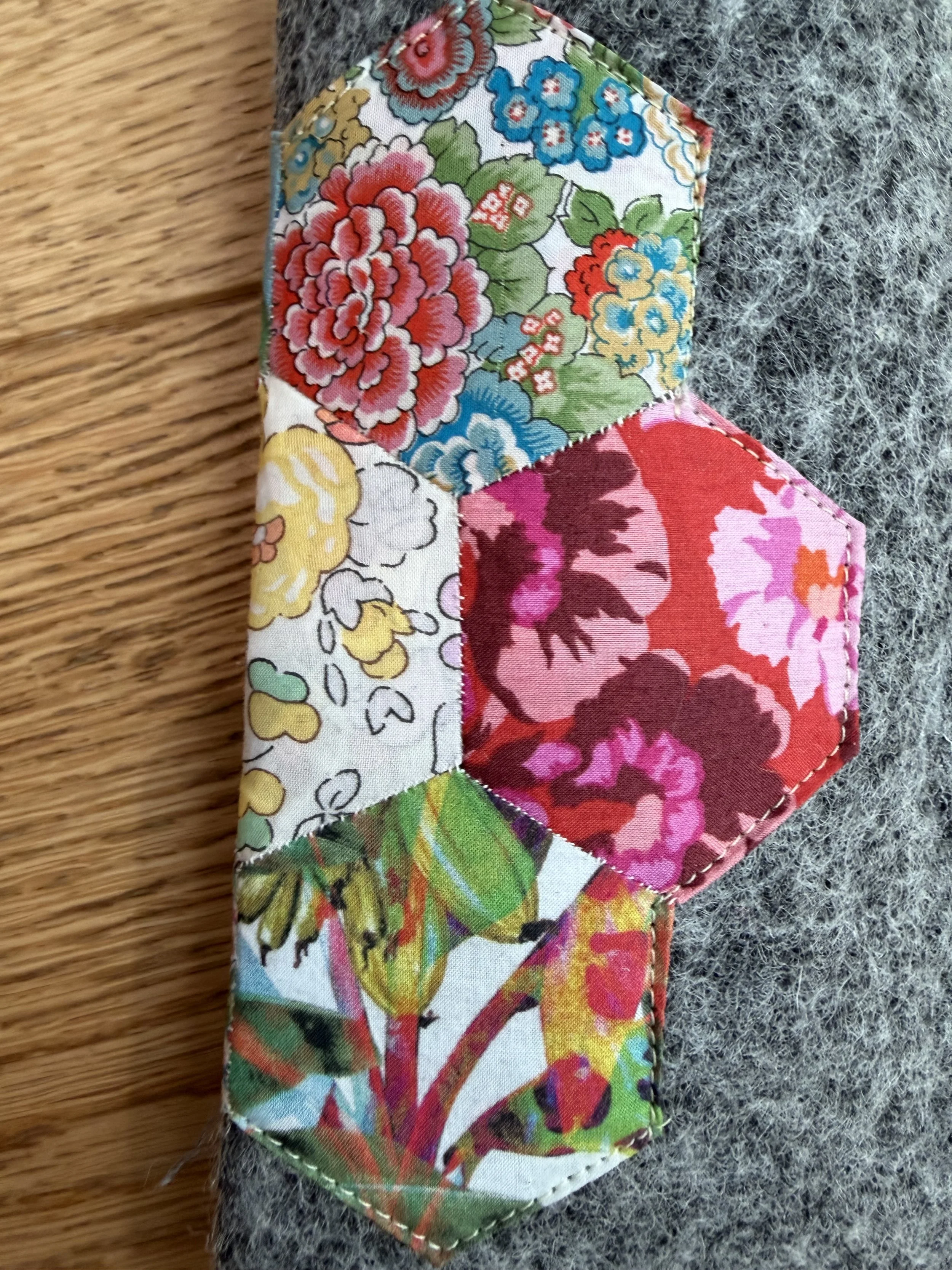Close-up of colourful Liberty Tana Lawn hexagons hand stitched onto grey wool glasses case