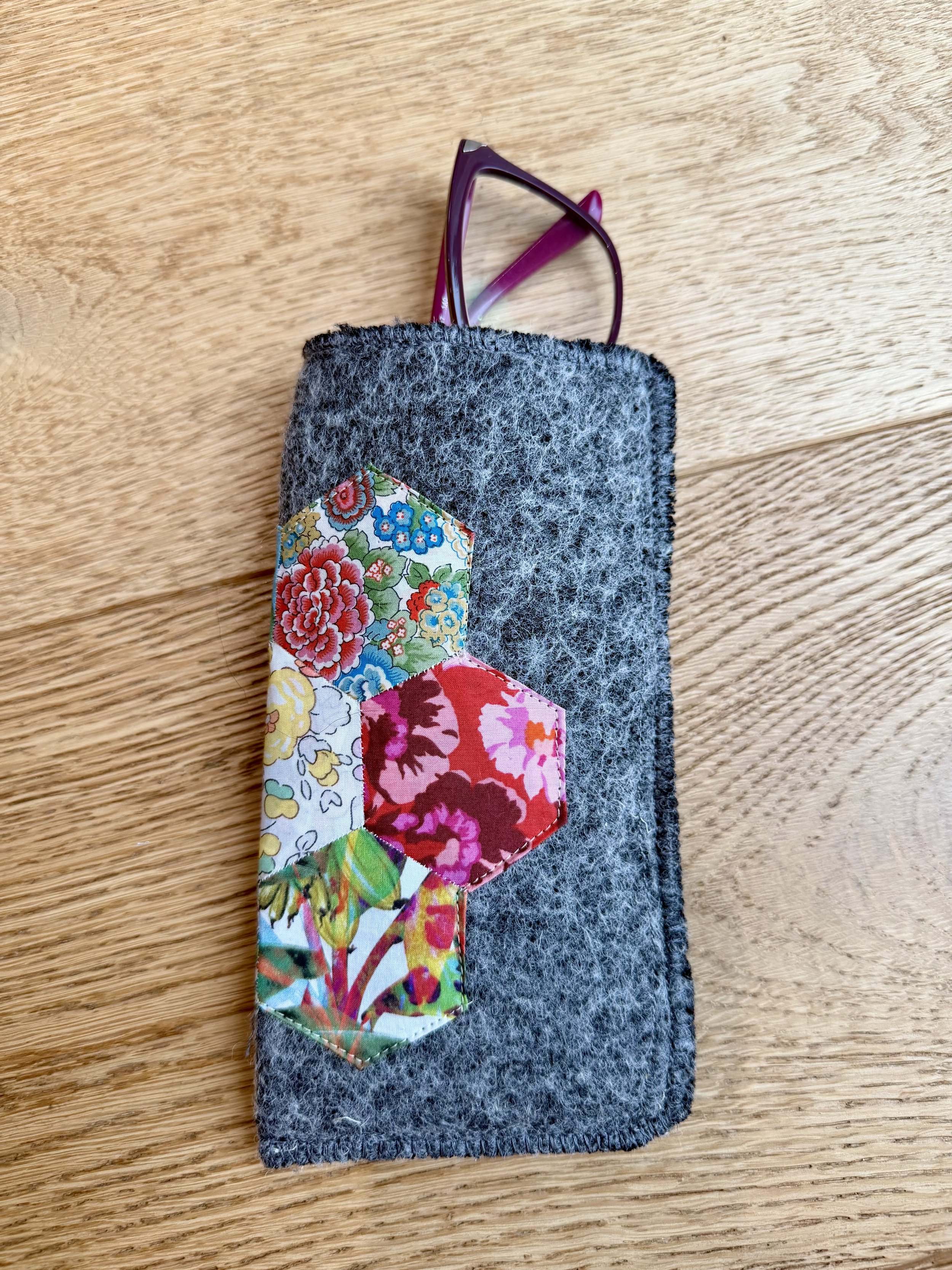 Grey wool Liberty Scrap Garden glasses case with colourful patchwork hexagons and purple glasses