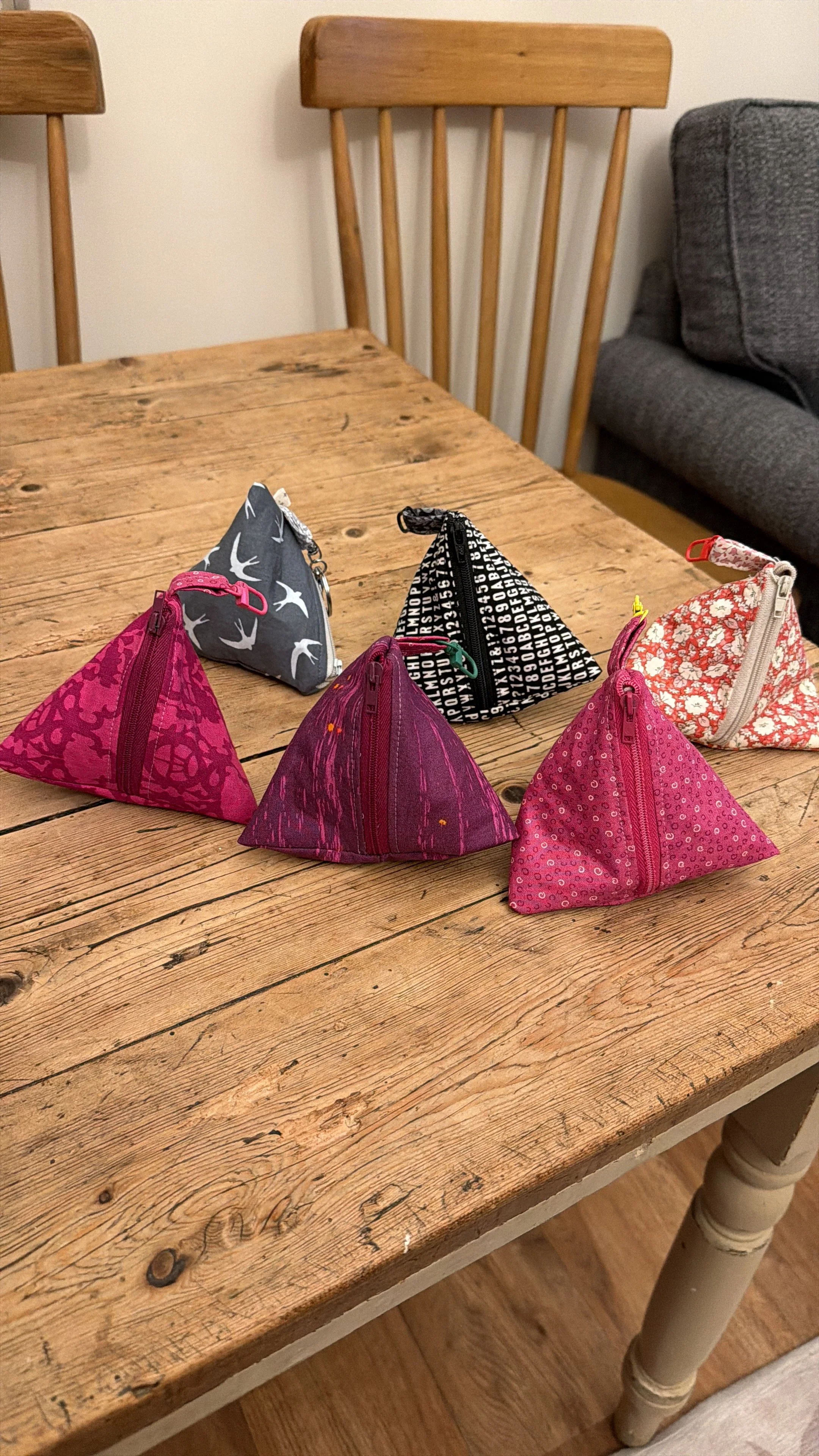 Six handmade Little Keeps triangle zip pouches in grey pink and black.