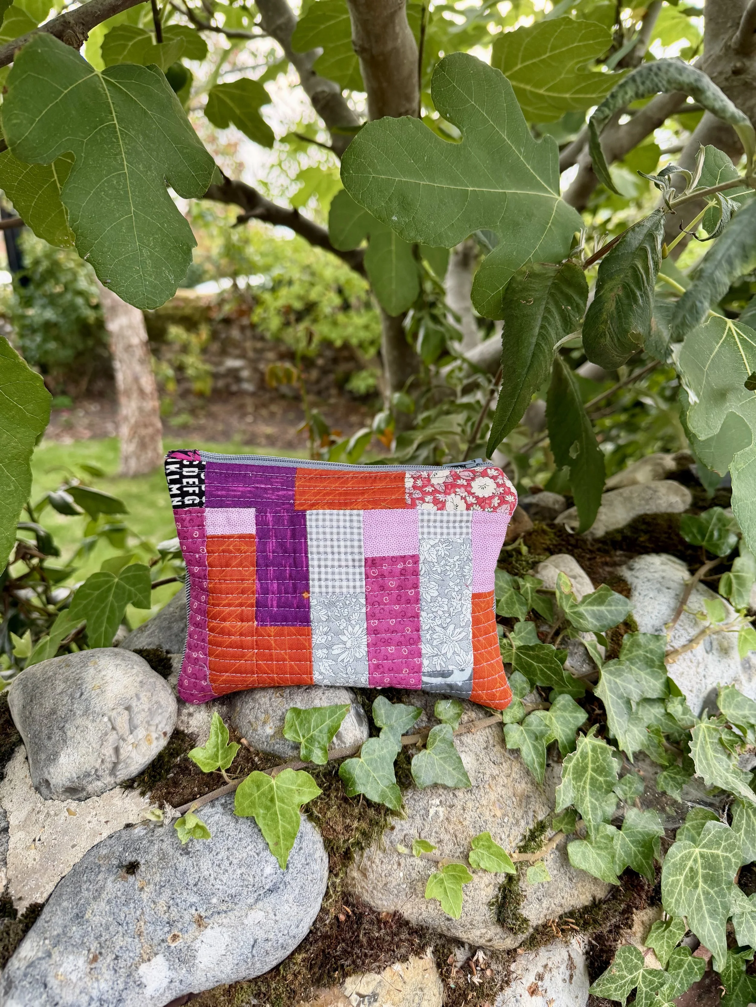 Berry and Clementine handmade patchwork pouch photographed amongst green fig leaves