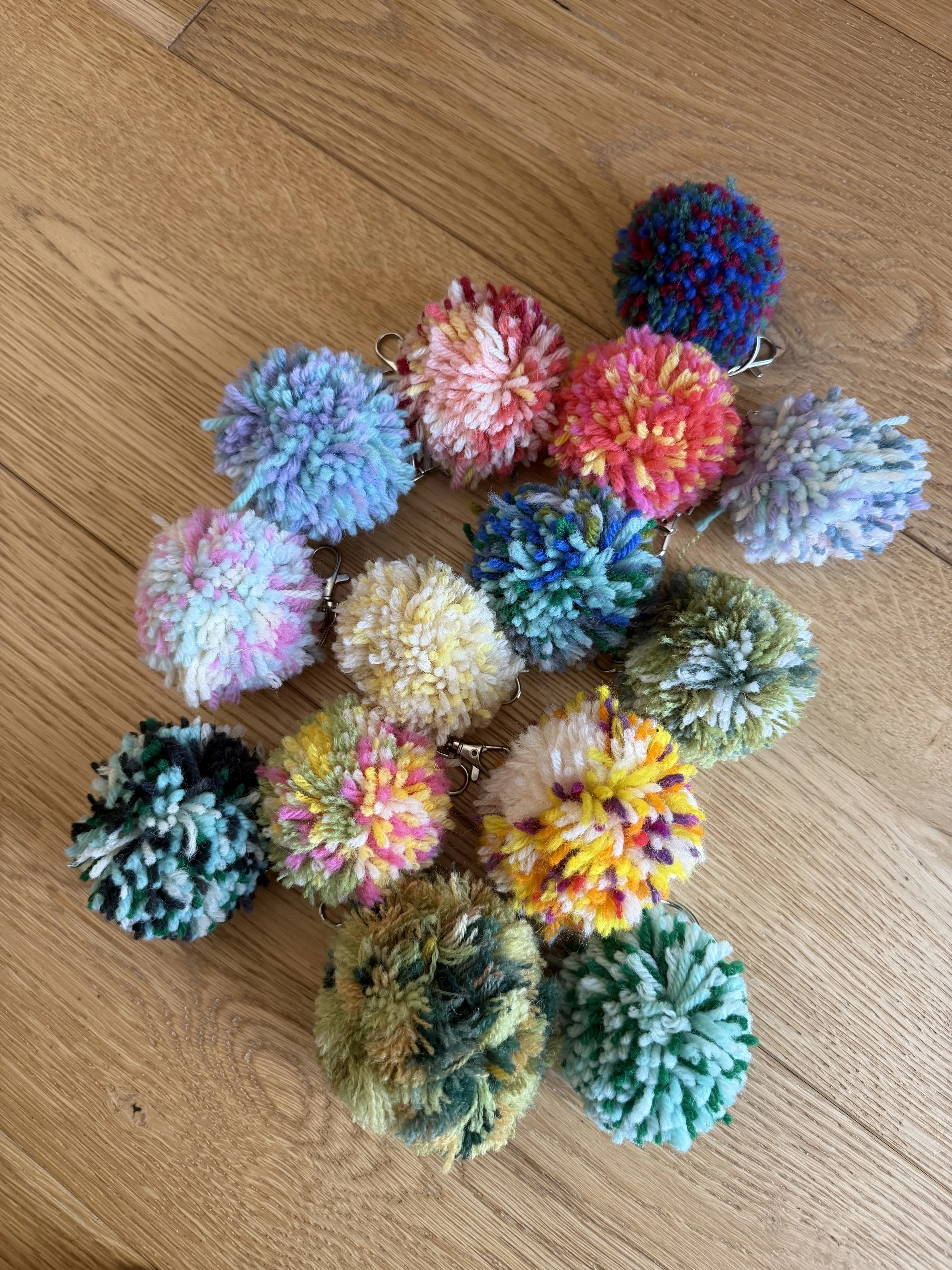 small group of  multicolour wool pom pom key ring with silver-coloured lobster clips on a wooden background.
