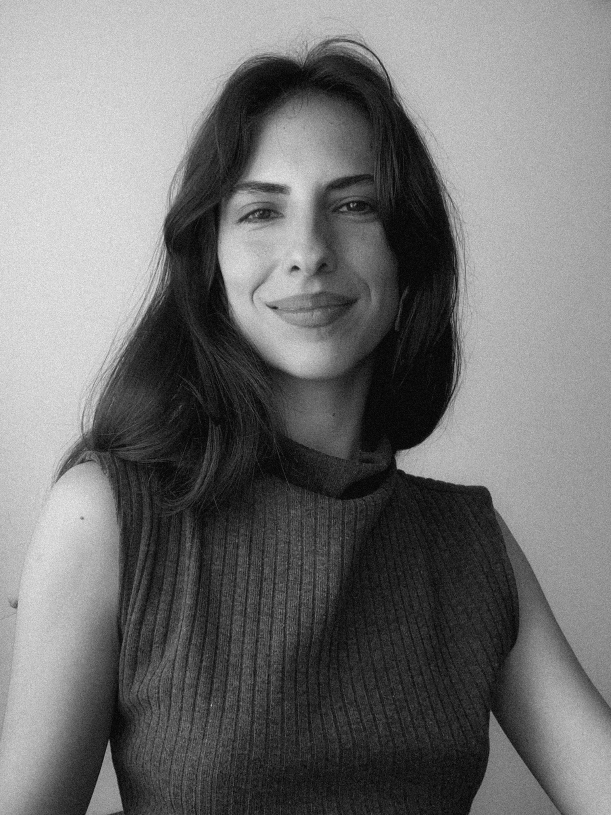 Retrato en blanco y negro de una mujer con cabello largo y oscuro, sonriendo ligeramente, usando un top de tela con rayas finas.