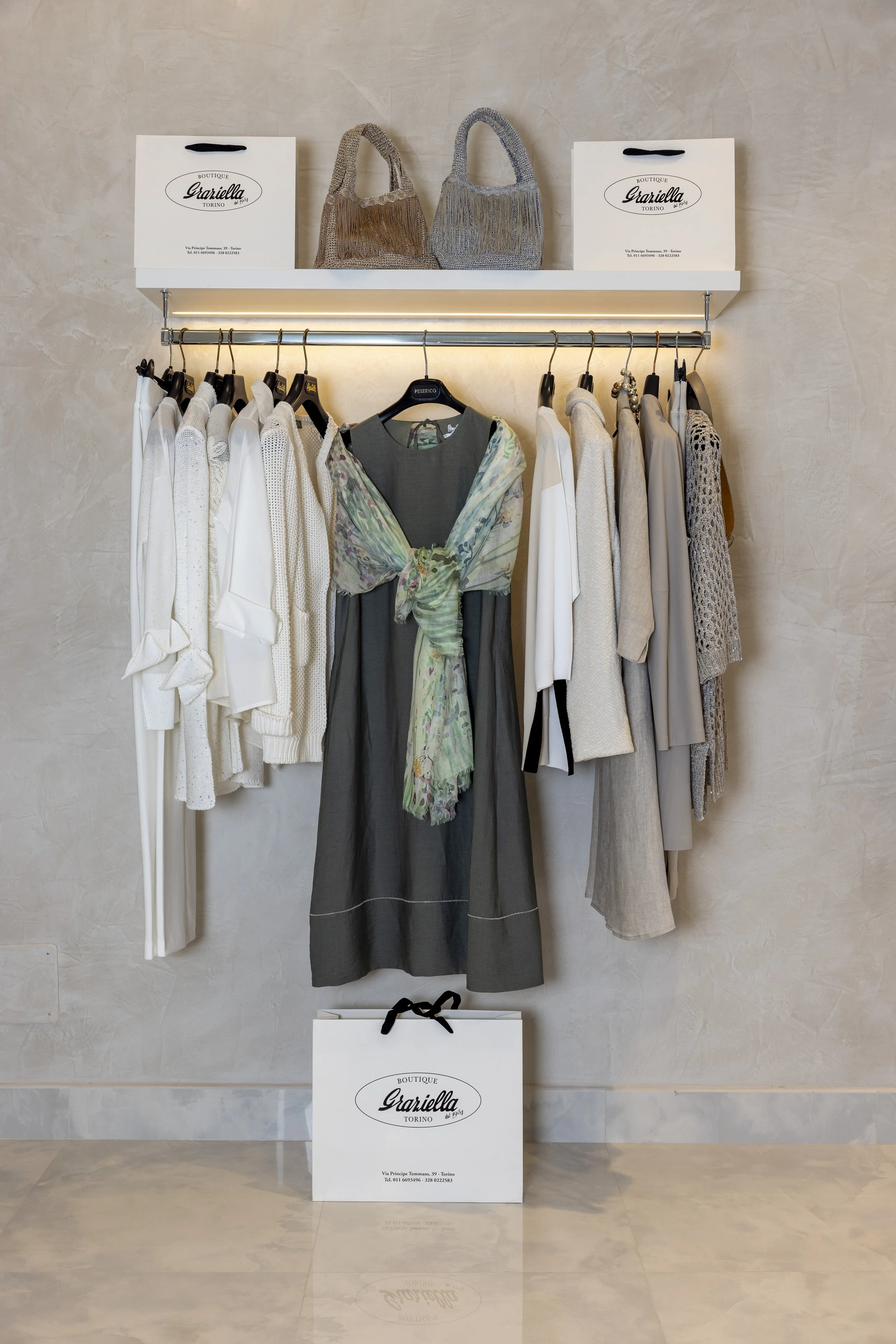 Abbigliamento femminile in vetrina, con capi di abbigliamento in tonalità neutre e accessori, e cartelloni pubblicitari con il logo 'Graziella Boutique Torino'.