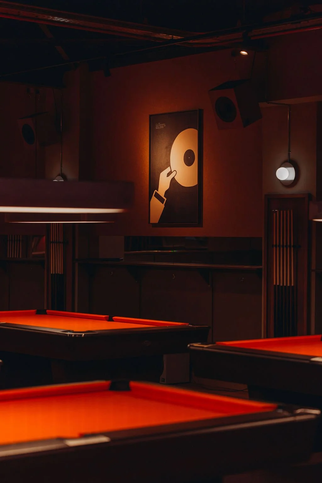 Dimly lit game room with pool tables and modern wall art featuring a hand holding a vinyl record.
