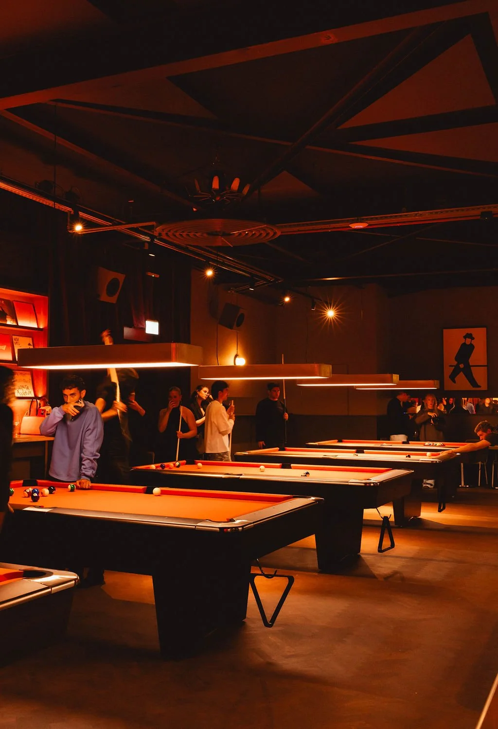 People playing pool in a dimly lit game room with orange lighting and modern decor.