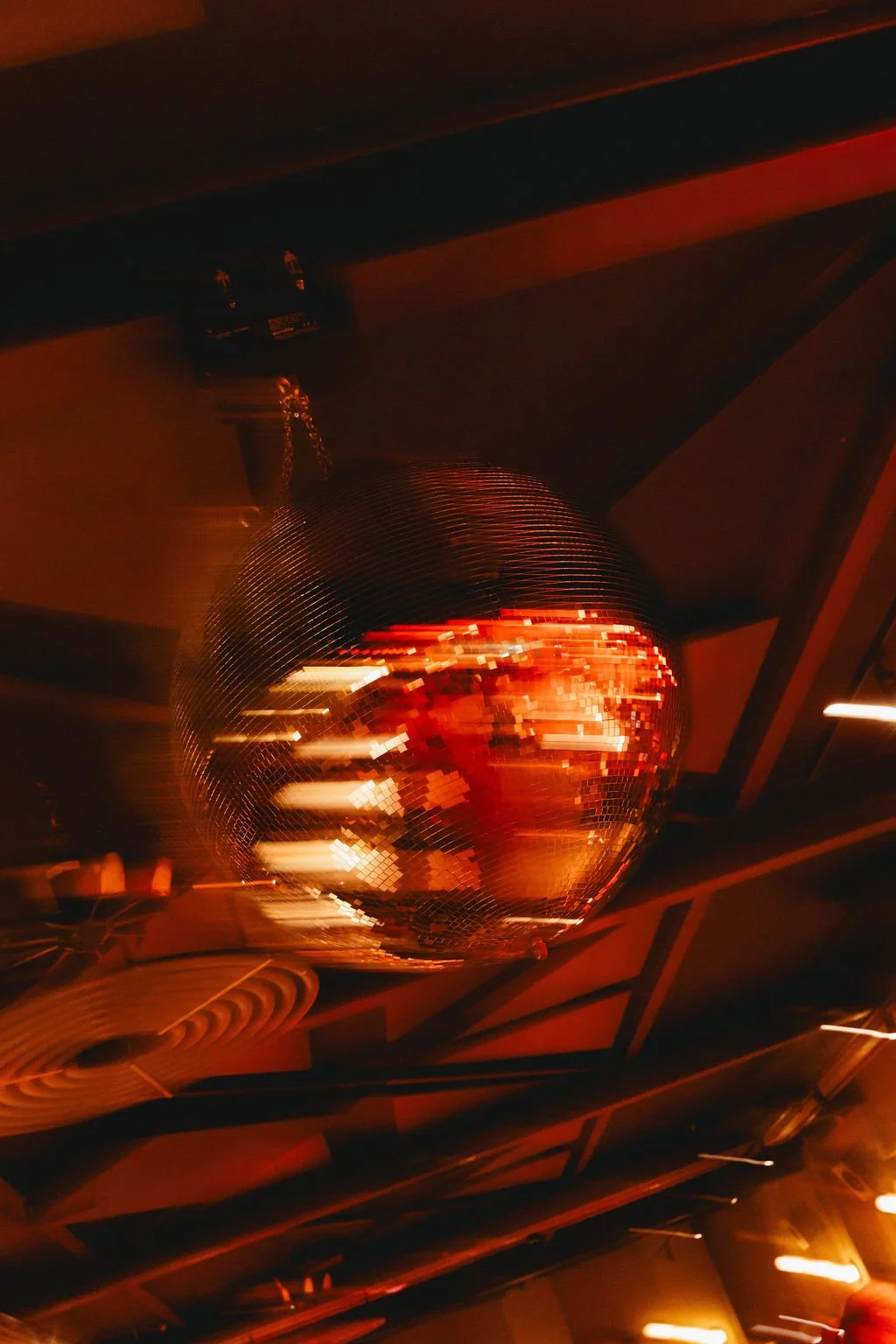 A large disco ball hanging from the ceiling reflecting lights in a dark, red-tinted room.