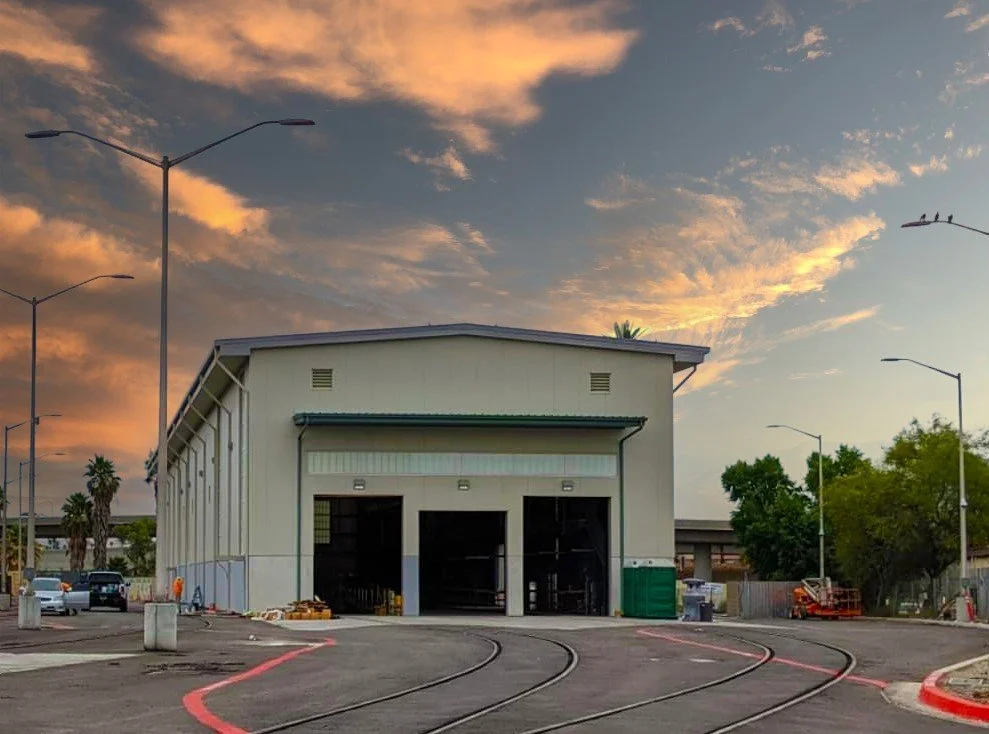Industrial warehouse with tram tracks, parking lot, and sunset sky.
