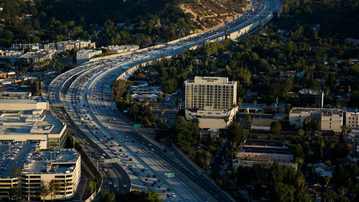Aerial view of a busy highway with many cars, surrounded by trees and buildings in an urban area
