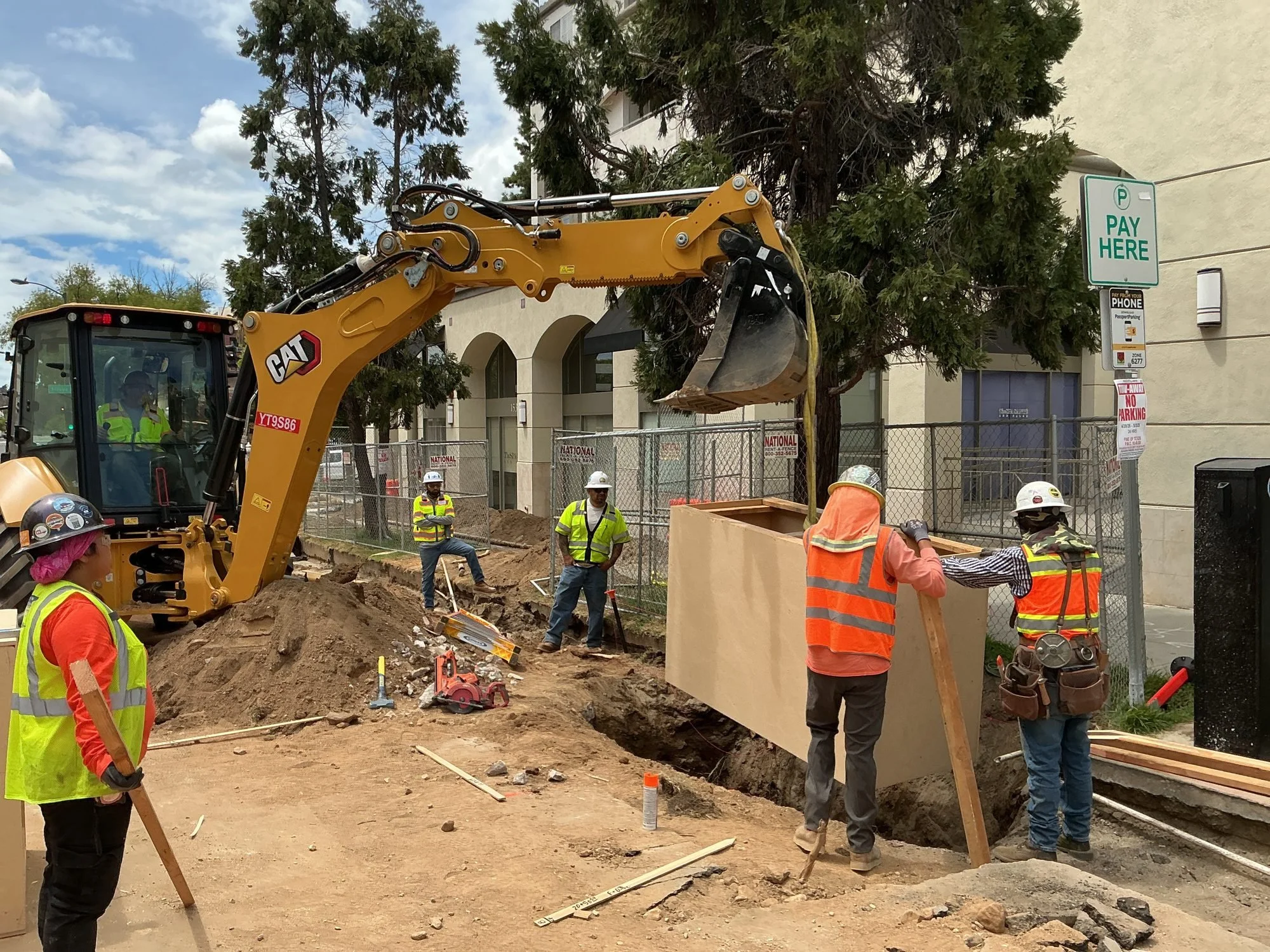 Construction site with workers and a yellow excavator digging a trench.