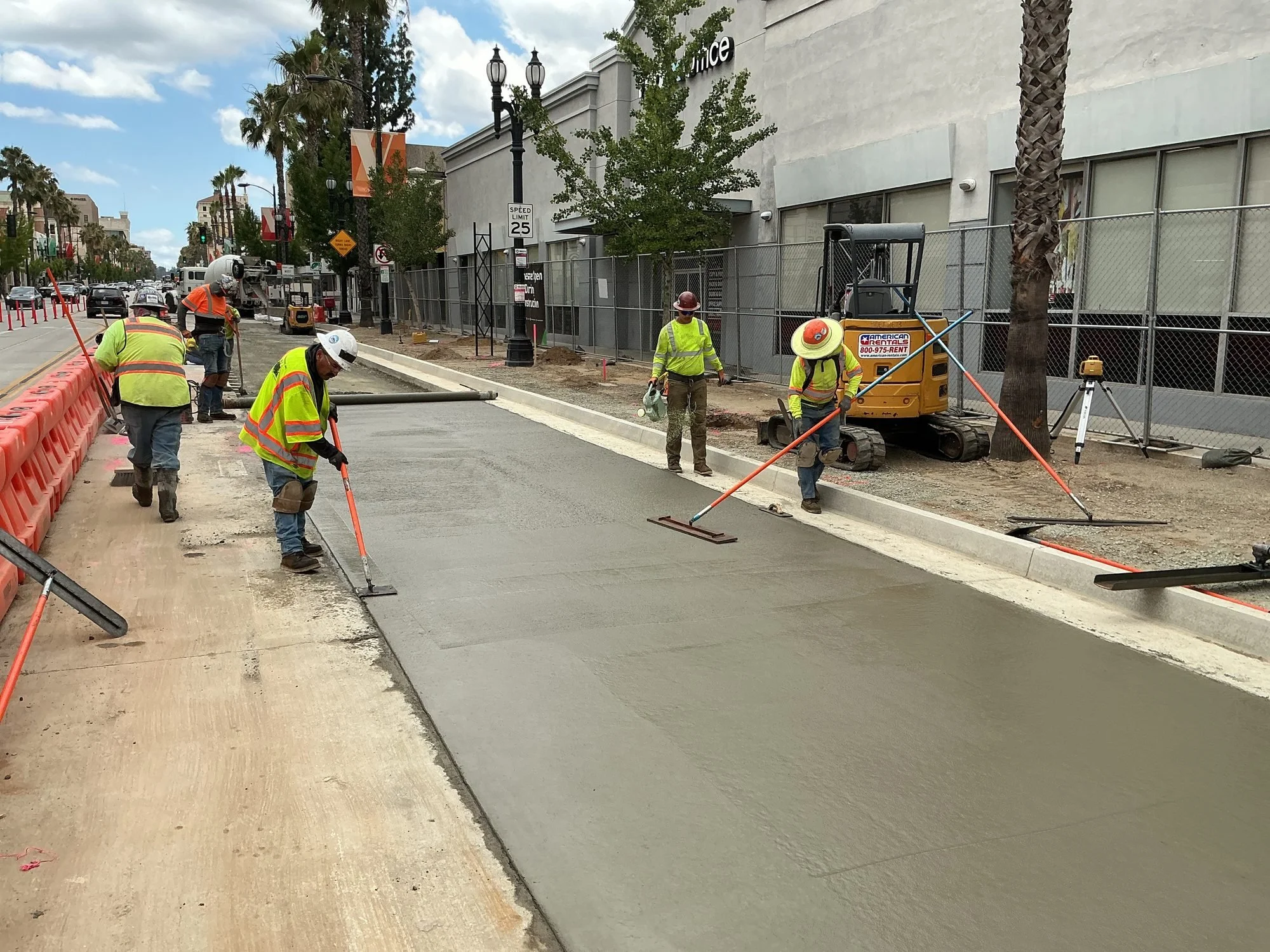 Construction workers laying down concrete on a city street, with construction equipment and safety barriers.