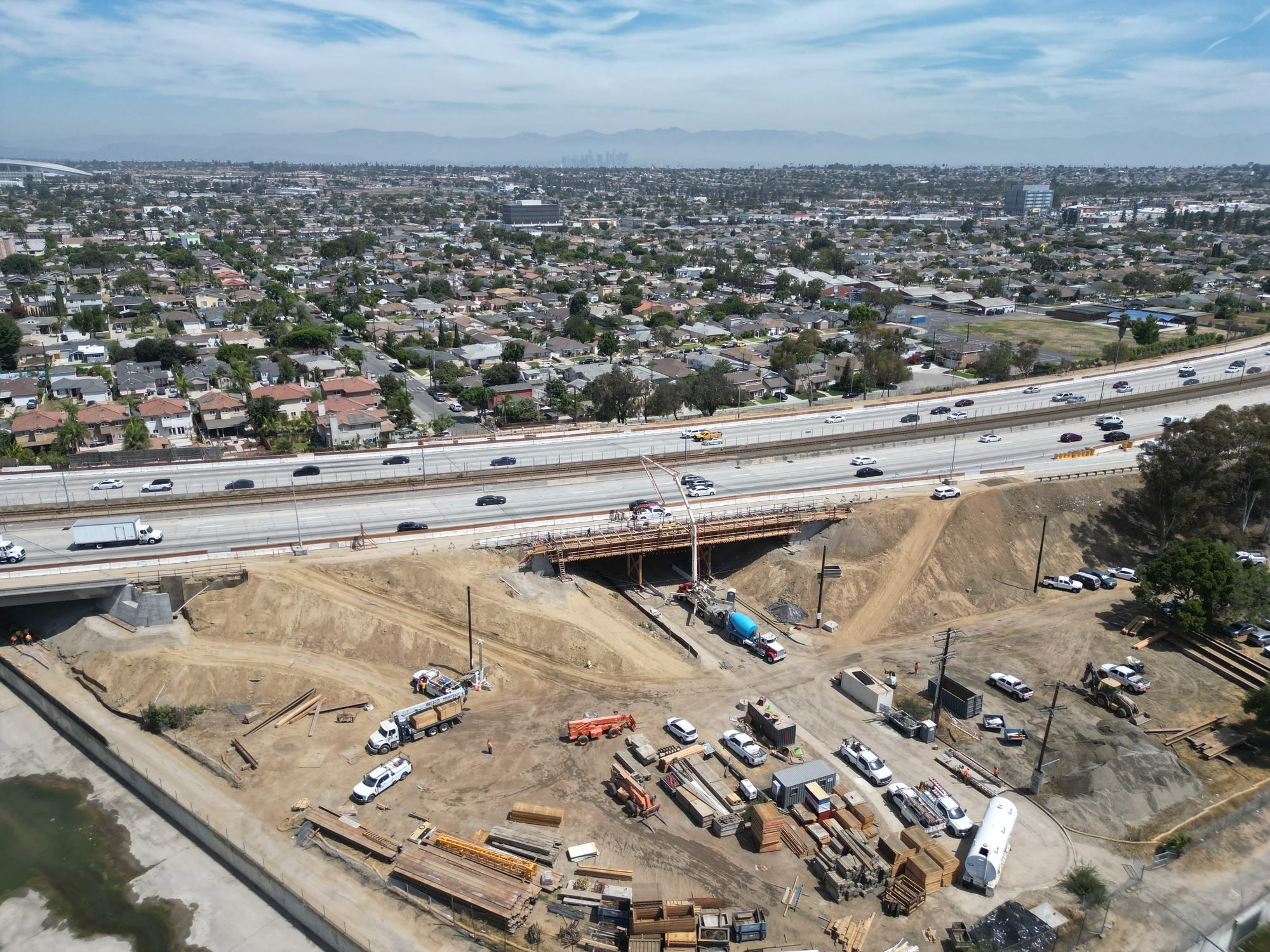 Aerial view of a cityscape with residential neighborhoods, a highway, and ongoing construction site with trucks, building materials, and equipment.