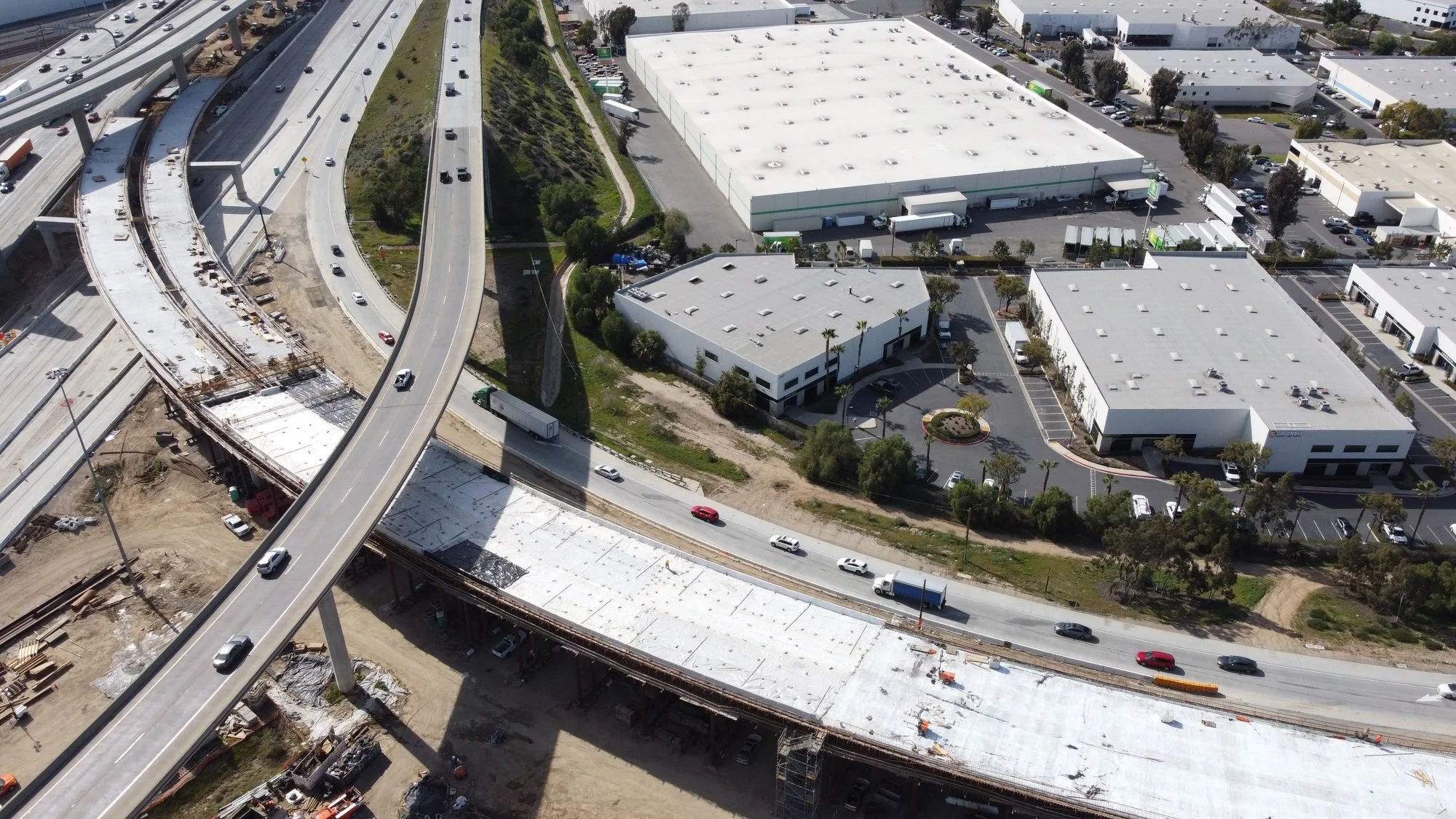 An aerial view showing multiple highway overpasses and a large commercial warehouse with surrounding parking lot and trees.
